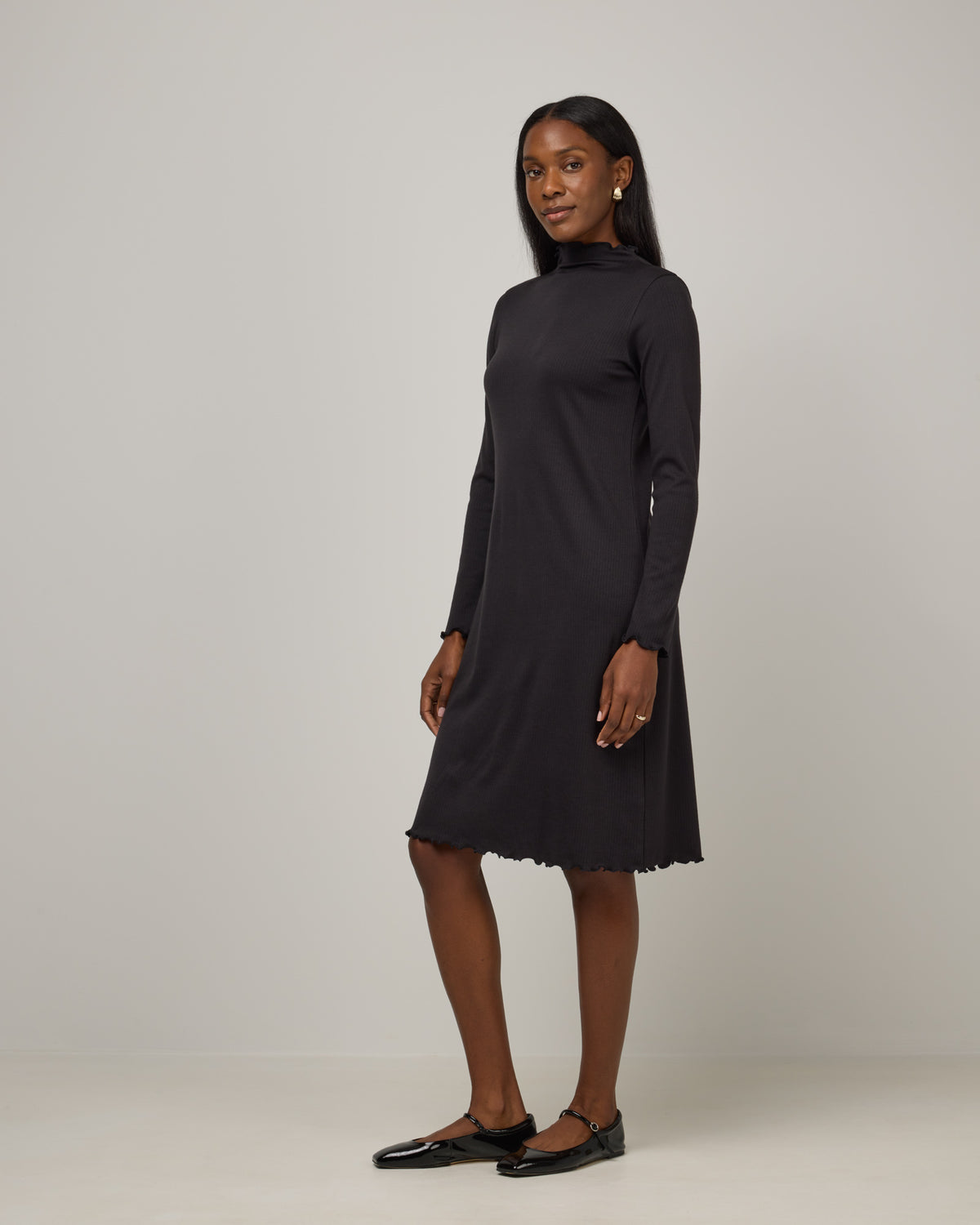 Model wearing Daphne Ribbed Dress in Black. Daphne Ribbed Dress is a merino wool long sleeve, turtleneck, knee length fitted dress available in sizes XS-XXL.