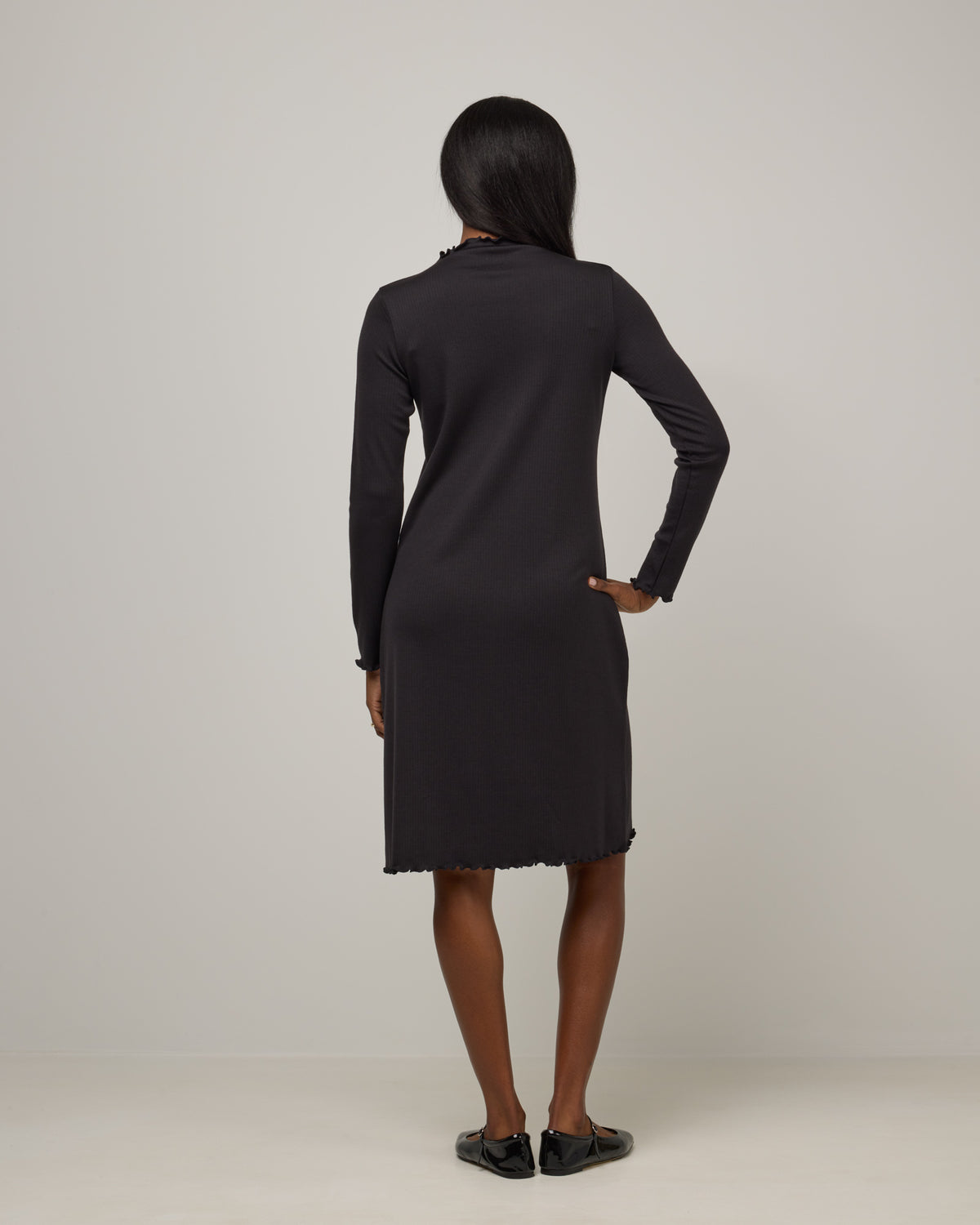 Model wearing Daphne Ribbed Dress in Black. Daphne Ribbed Dress is a merino wool long sleeve, turtleneck, knee length fitted dress available in sizes XS-XXL.