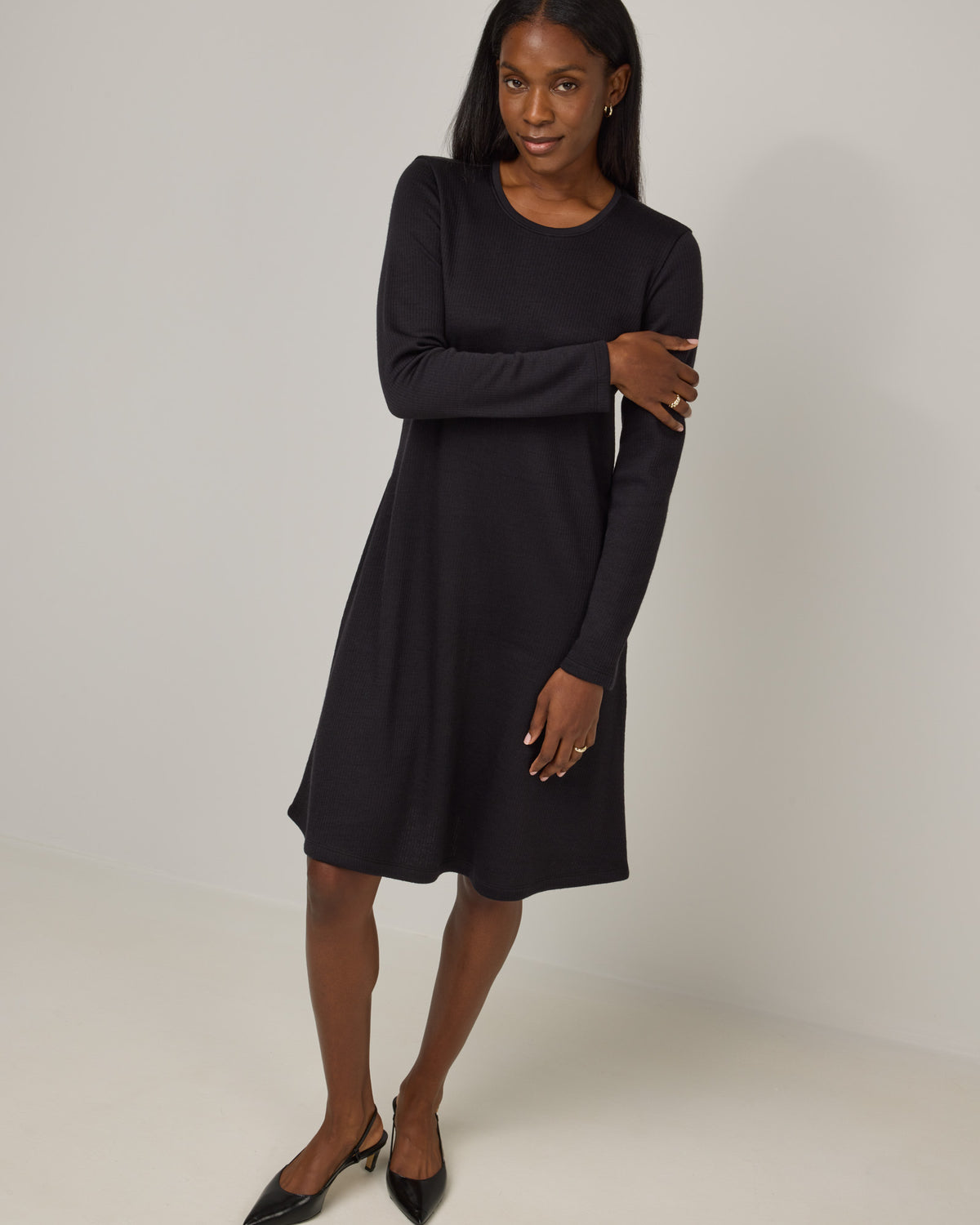Model wearing Bethany Double Knit Ribbed Dress in Black. Bethany Double Knit Ribbed Dress is a merino wool long sleeve, crew neck, midi swing dress with pockets available in sizes XS-3X.