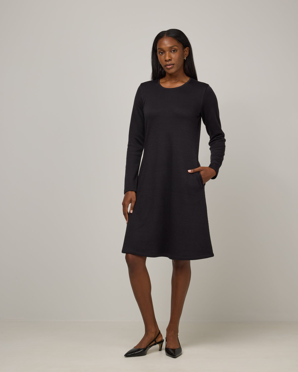 Model wearing Bethany Double Knit Ribbed Dress in Black. Bethany Double Knit Ribbed Dress is a merino wool long sleeve, crew neck, midi swing dress with pockets available in sizes XS-3X.