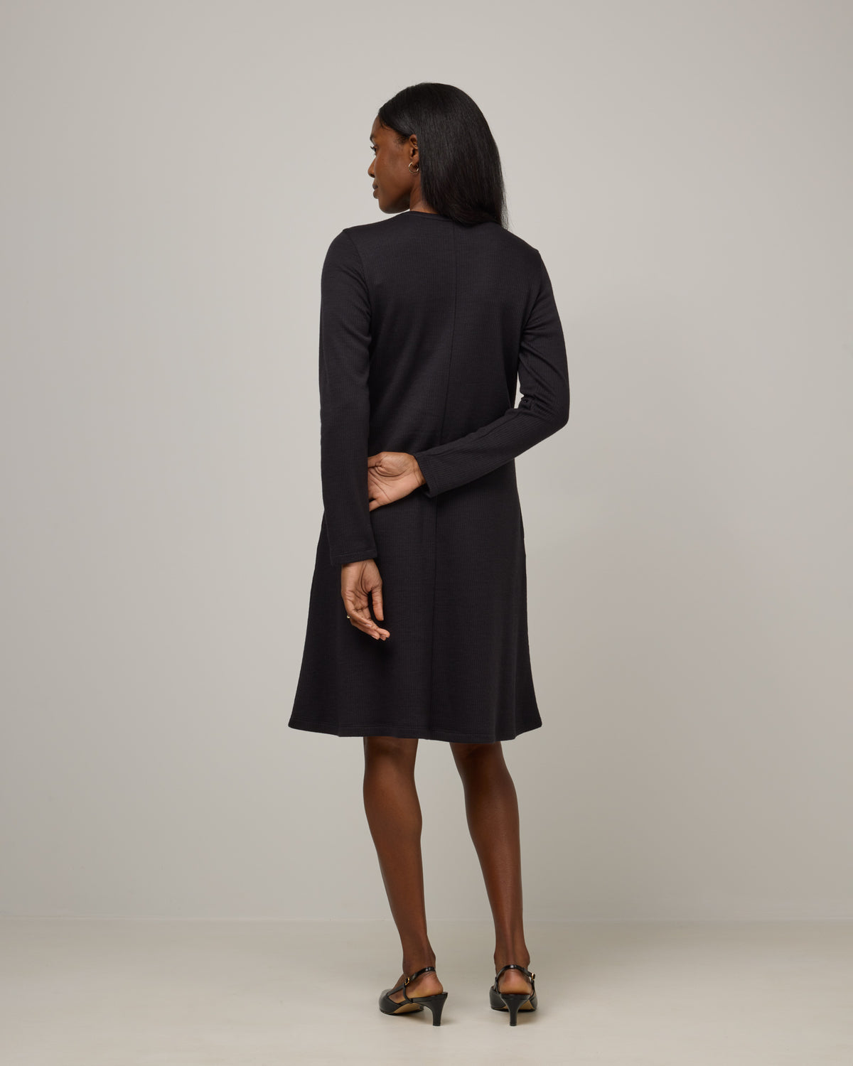 Model wearing Bethany Double Knit Ribbed Dress in Black. Bethany Double Knit Ribbed Dress is a merino wool long sleeve, crew neck, midi swing dress with pockets available in sizes XS-3X.
