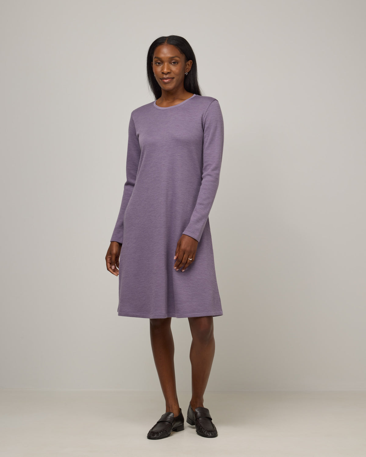 Model wearing Bethany Double Knit Ribbed Dress in Purple Sage, a soft, muted purple color. Bethany Double Knit Ribbed Dress is a merino wool long sleeve, crew neck, midi swing dress with pockets available in sizes XS-3X.