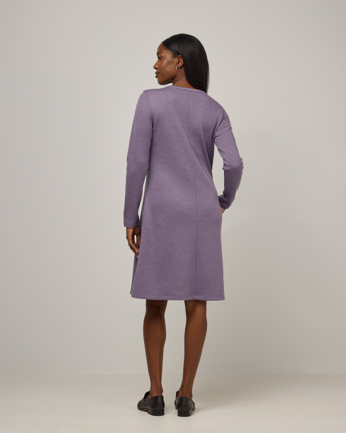 Model wearing Bethany Double Knit Ribbed Dress in Purple Sage, a soft, muted purple color. Bethany Double Knit Ribbed Dress is a merino wool long sleeve, crew neck, midi swing dress with pockets available in sizes XS-3X.