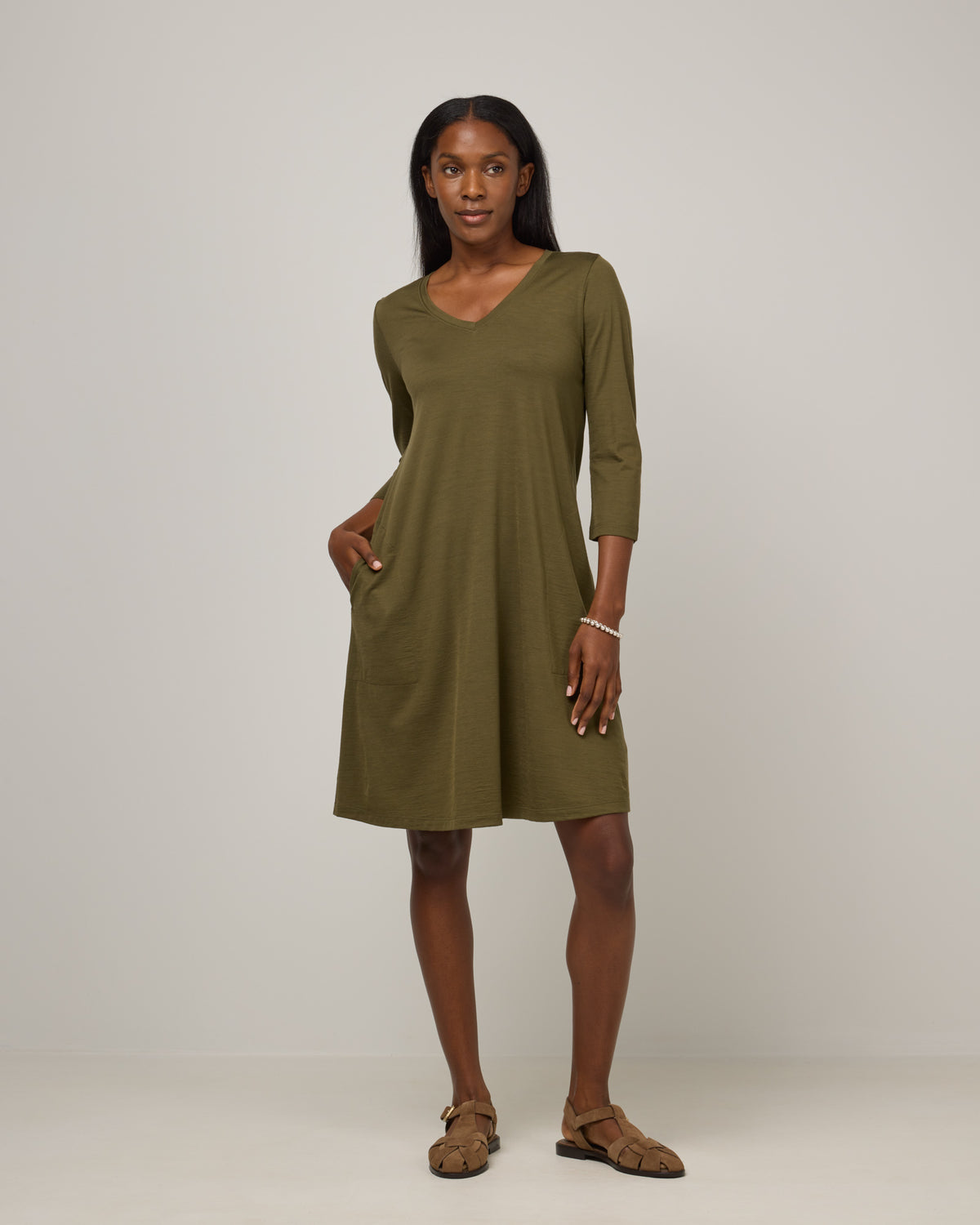 Model wearing Willow Swing Dress in Olive. Willow Swing Dress is a merino wool long sleeve, v-neck, knee length swing dress with pockets available in sizes XS-3X Regular, XS-3X Long.