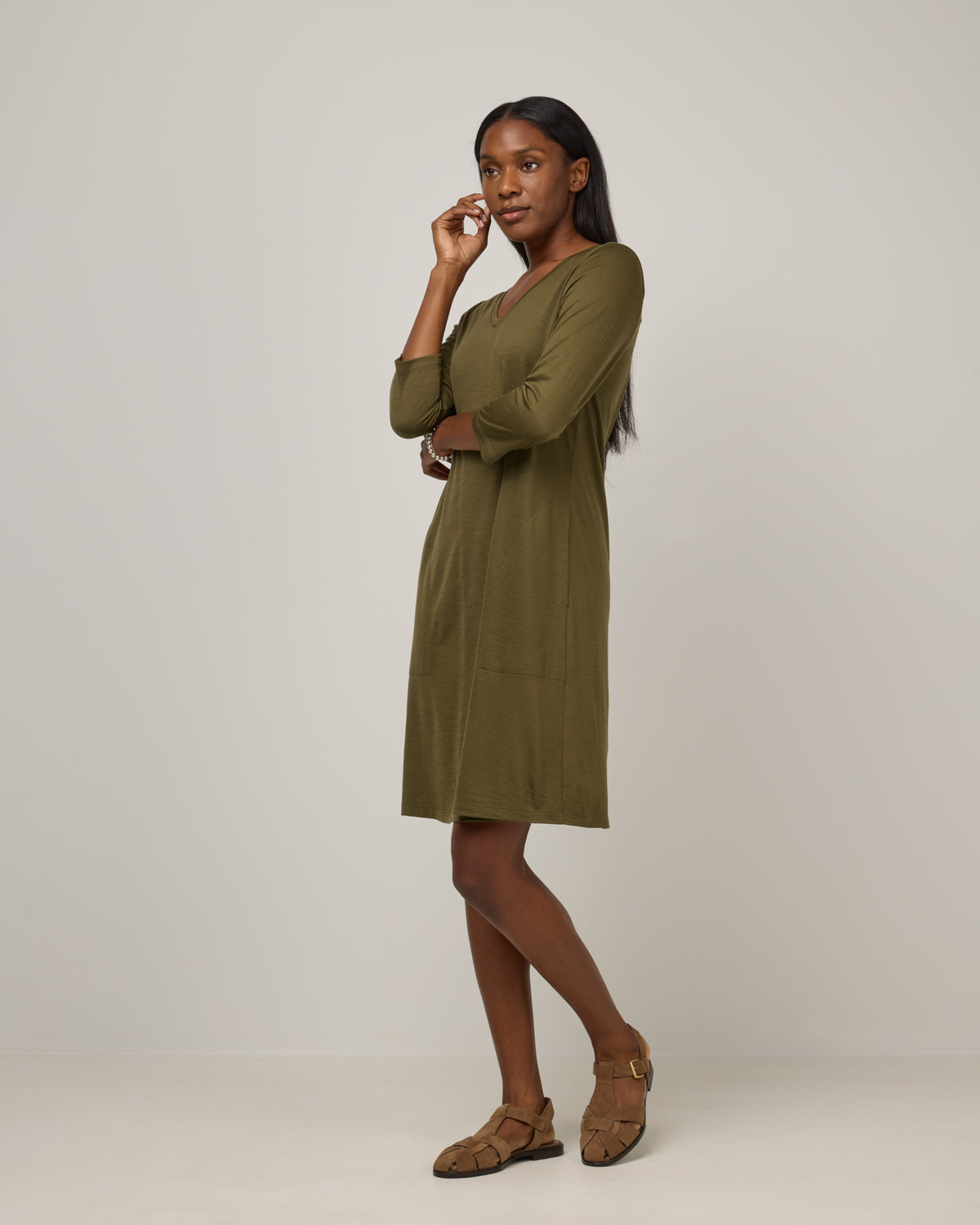 Model wearing Willow Swing Dress in Olive. Willow Swing Dress is a merino wool long sleeve, v-neck, knee length swing dress with pockets available in sizes XS-3X Regular, XS-3X Long.