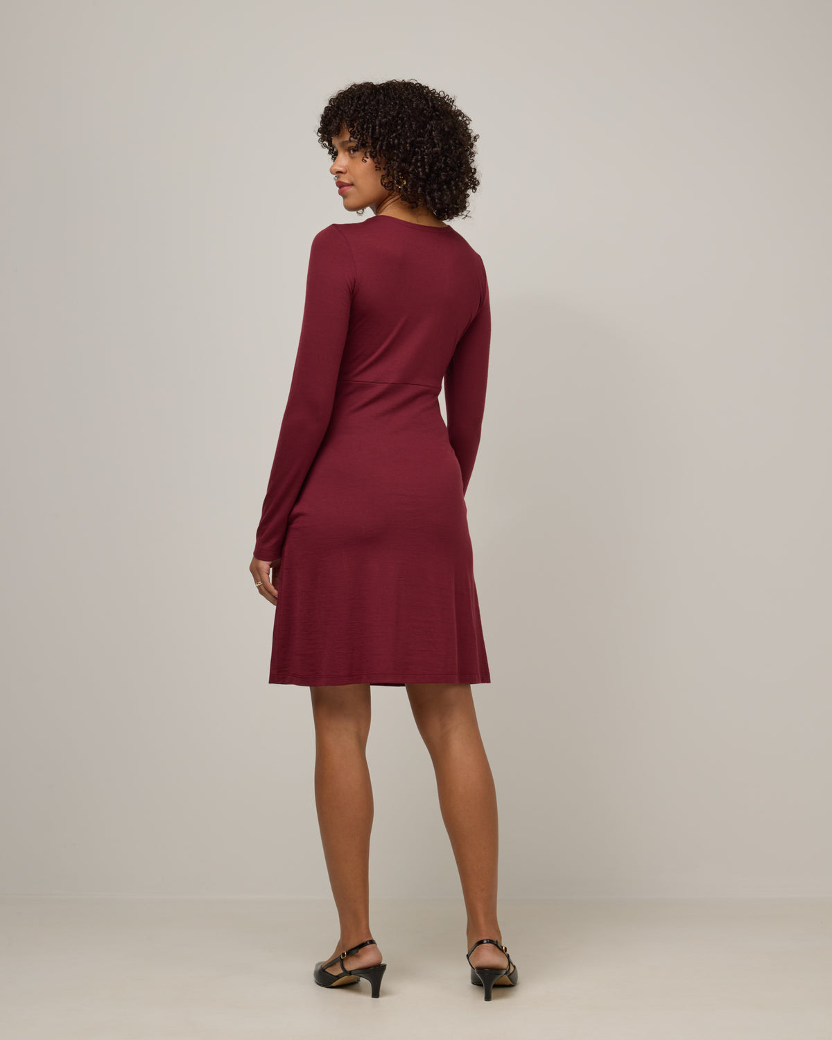 Model wearing Nova Twist Front Dress in Burgundy. Nova Twist Front Dress is a merino wool long sleeve, crew neck, knee length fit & flare dress with pockets available in sizes XS-3X.