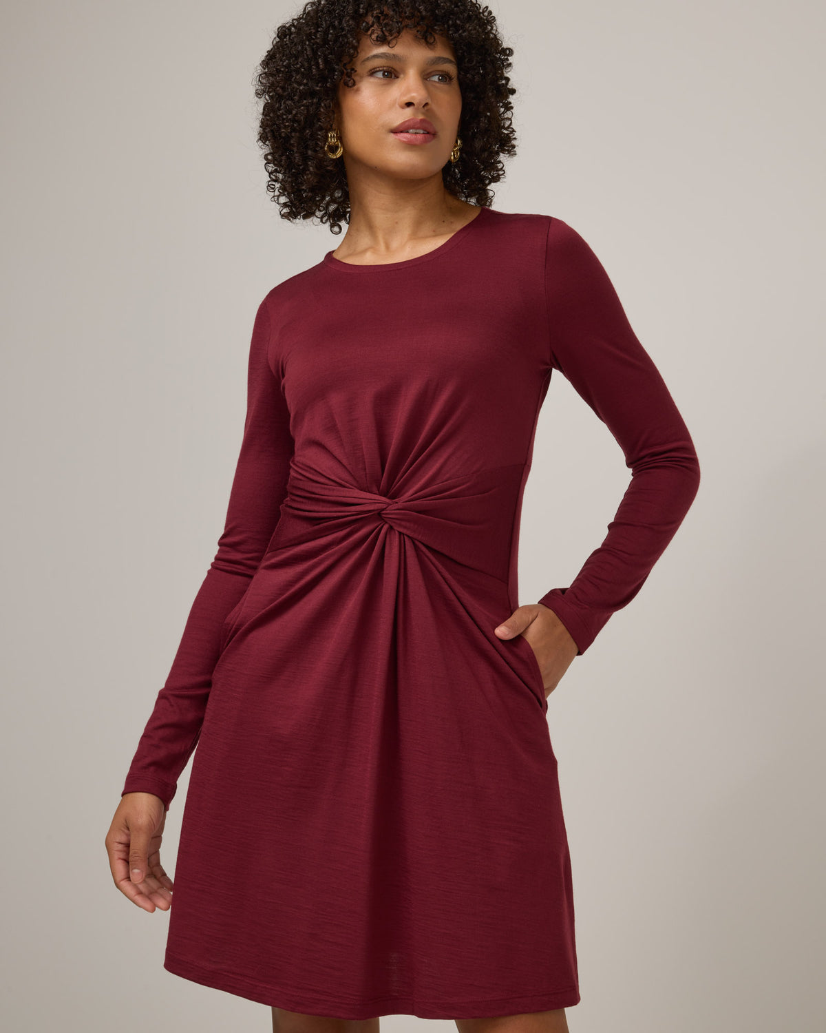 Model wearing Nova Twist Front Dress in Burgundy. Nova Twist Front Dress is a merino wool long sleeve, crew neck, knee length fit & flare dress with pockets available in sizes XS-3X.