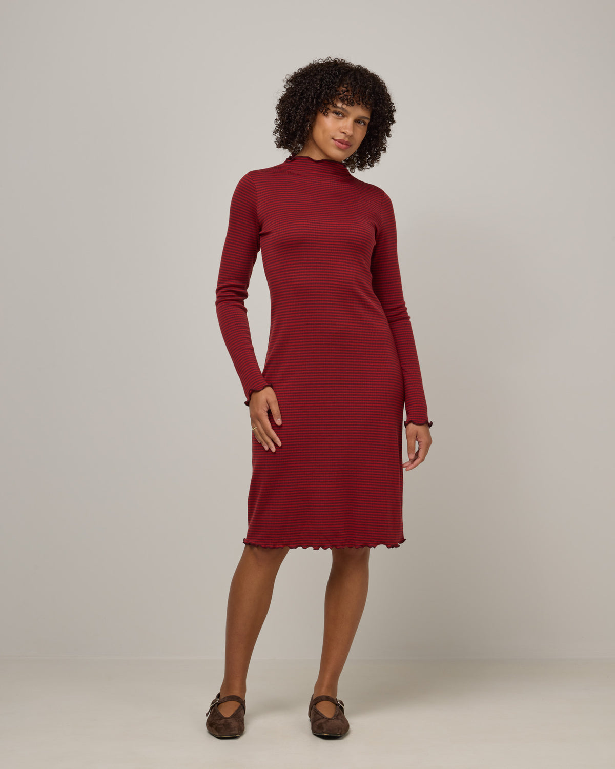 Model wearing Daphne Ribbed Dress in Burgundy & Modern Red Stripe. Daphne Ribbed Dress is a merino wool long sleeve, turtleneck, knee length fitted dress available in sizes XS-XXL.