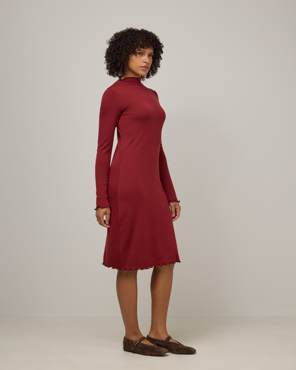 Model wearing Daphne Ribbed Dress in Burgundy & Modern Red Stripe. Daphne Ribbed Dress is a merino wool long sleeve, turtleneck, knee length fitted dress available in sizes XS-XXL.