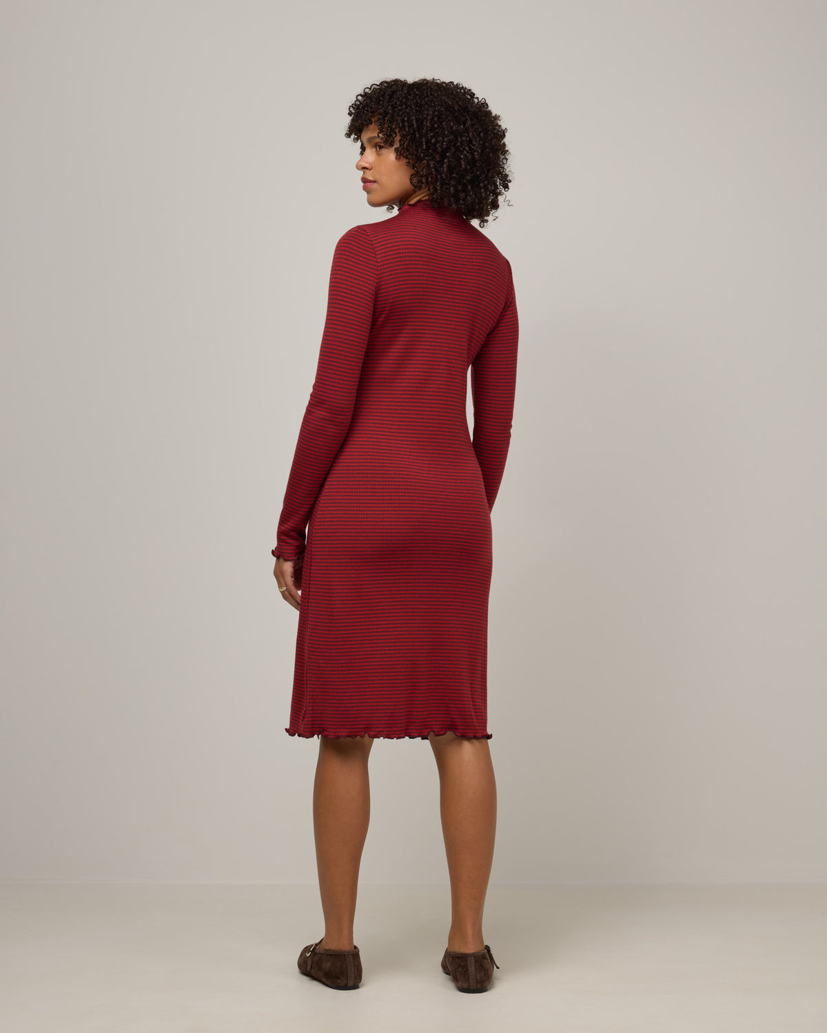 Model wearing Daphne Ribbed Dress in Burgundy & Modern Red Stripe. Daphne Ribbed Dress is a merino wool long sleeve, turtleneck, knee length fitted dress available in sizes XS-XXL.