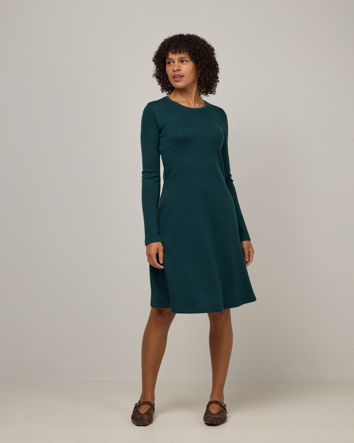 Model wearing Bethany Double Knit Ribbed Dress in Pine, a saturated forest green color. Bethany Double Knit Ribbed Dress is a merino wool long sleeve, crew neck, midi swing dress with pockets available in sizes XS-3X.