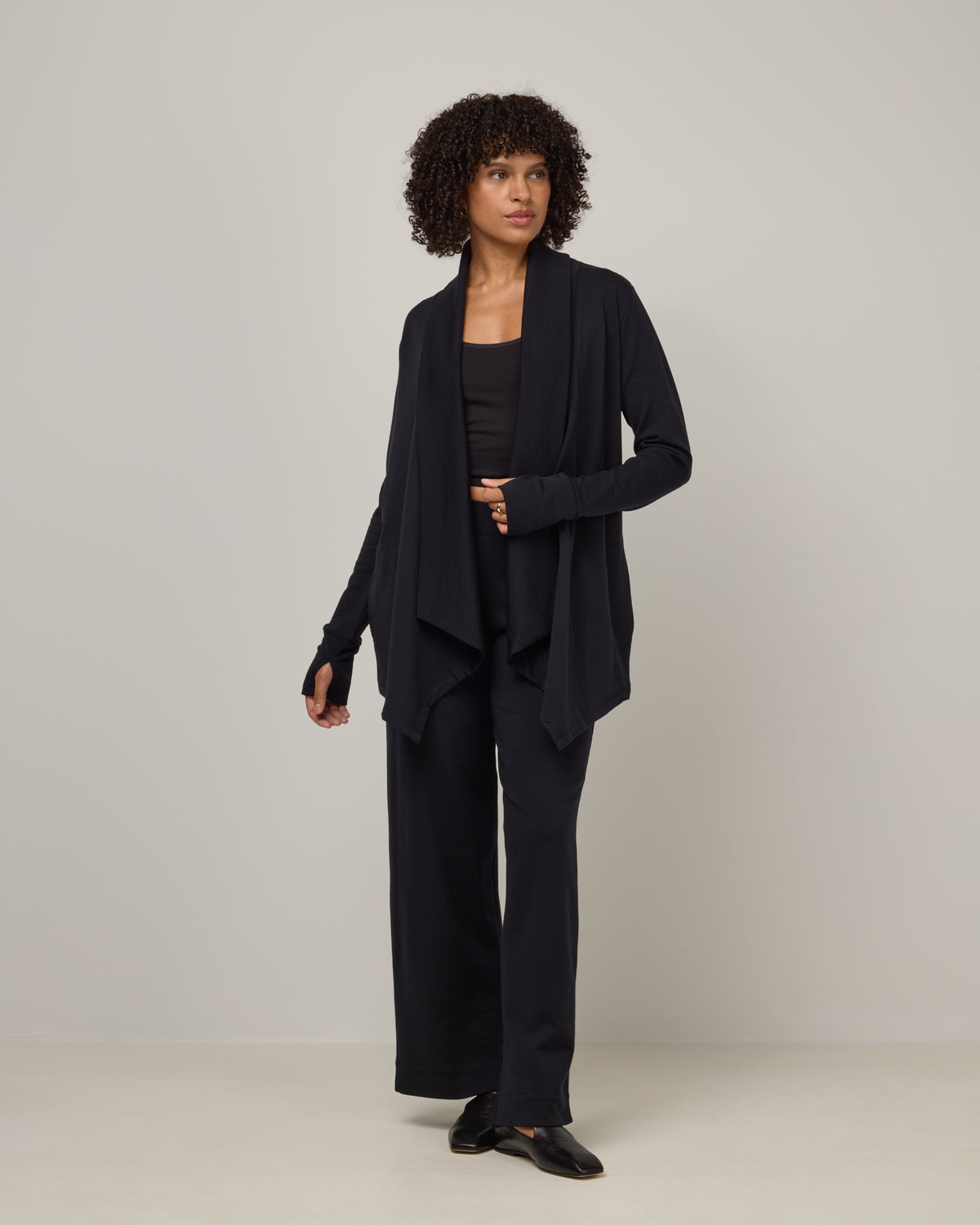 Model wearing Aspen Cardigan in Black. Aspen Cardigan is a merino wool long sleevecardigan with pockets available in sizes XS-3X.