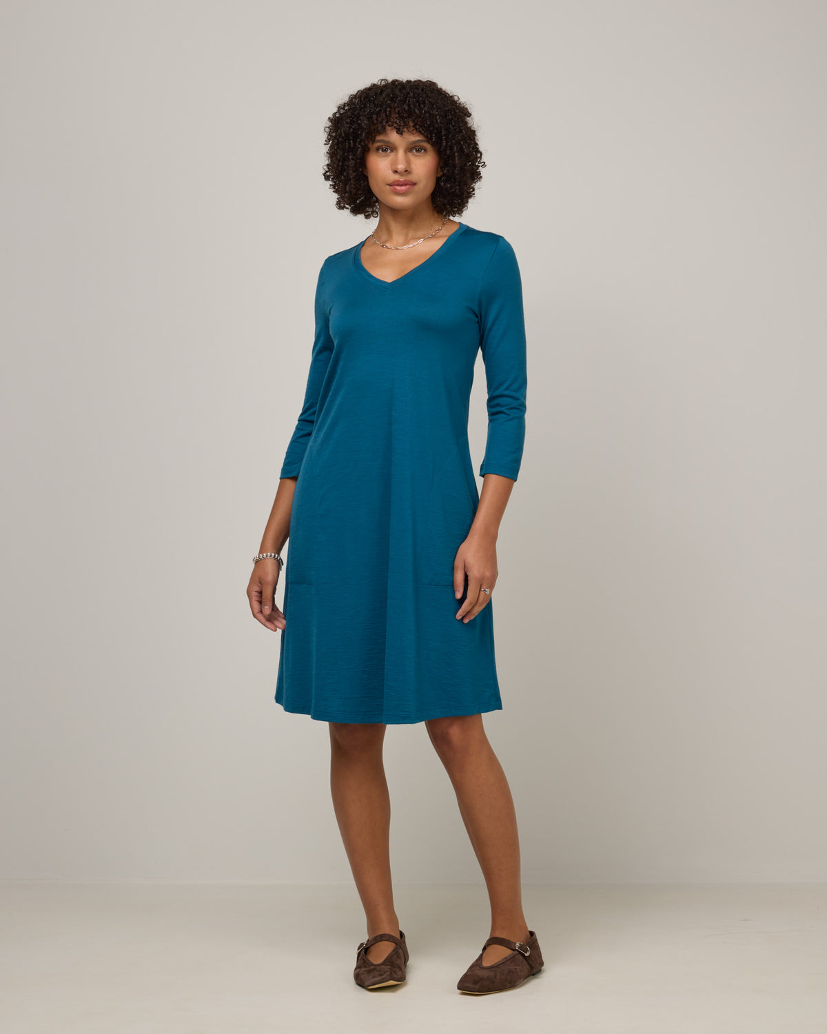Model wearing Willow Swing Dress in Ocean Teal, a medium blue-green color. Willow Swing Dress is a merino wool long sleeve, v-neck, knee length swing dress with pockets available in sizes XS-3X Regular, XS-3X Long.