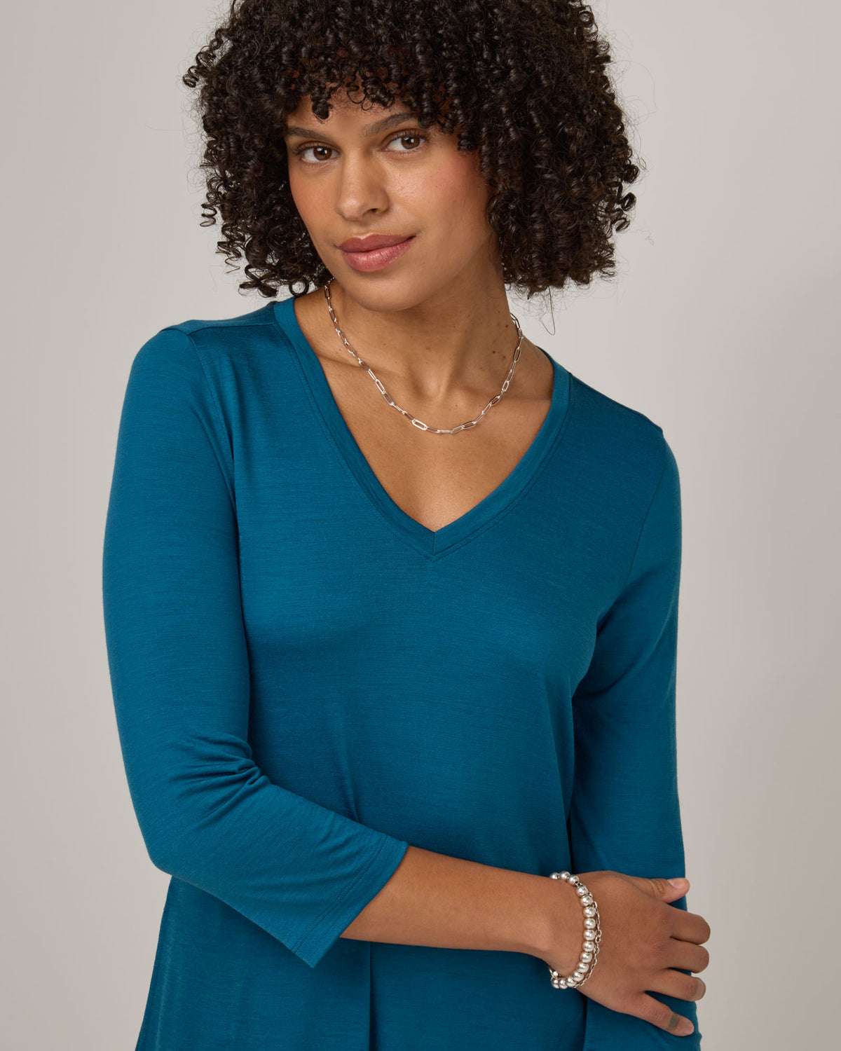 Model wearing Willow Swing Dress in Ocean Teal, a medium blue-green color. Willow Swing Dress is a merino wool long sleeve, v-neck, knee length swing dress with pockets available in sizes XS-3X Regular, XS-3X Long.