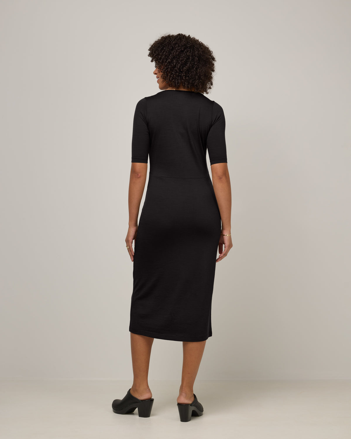 Model wearing London Fitted Dress in Black. London Fitted Dress is a merino wool short sleeve, v-neck, midi fitted dress available in sizes XS-3X Regular, XS-XL Petite.