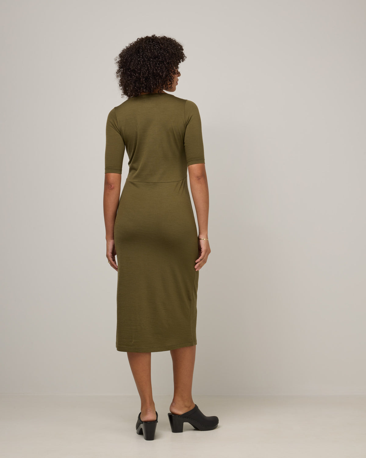 Model wearing London Fitted Dress in Olive. London Fitted Dress is a merino wool short sleeve, v-neck, midi fitted dress available in sizes XS-3X Regular, XS-XL Petite.