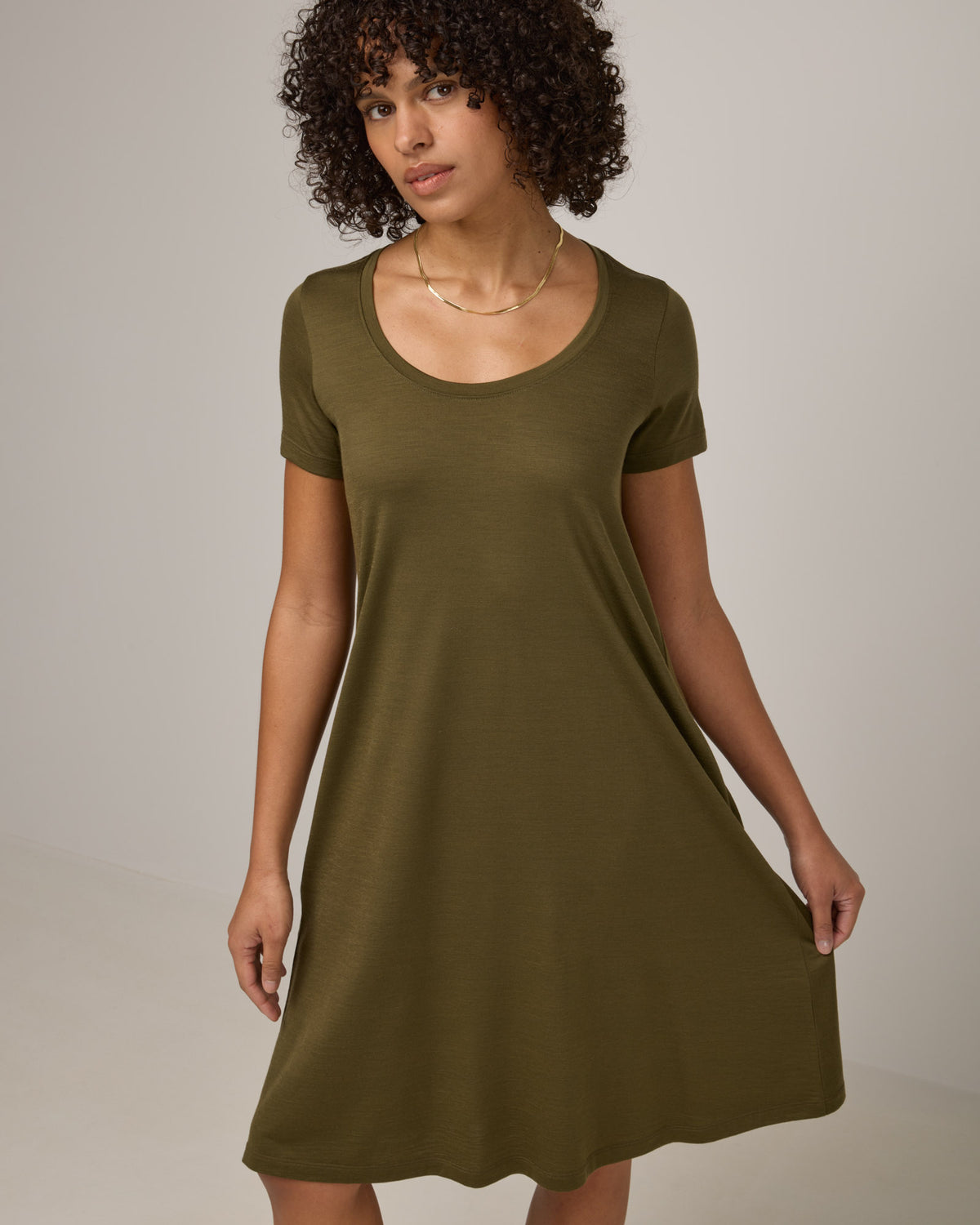 Model wearing Maggie Swing Dress in Olive. Maggie Swing Dress is a merino wool short sleeve, scoop neck, knee length swing dress with pockets available in sizes XS-3X Regular, XS-3X Long.