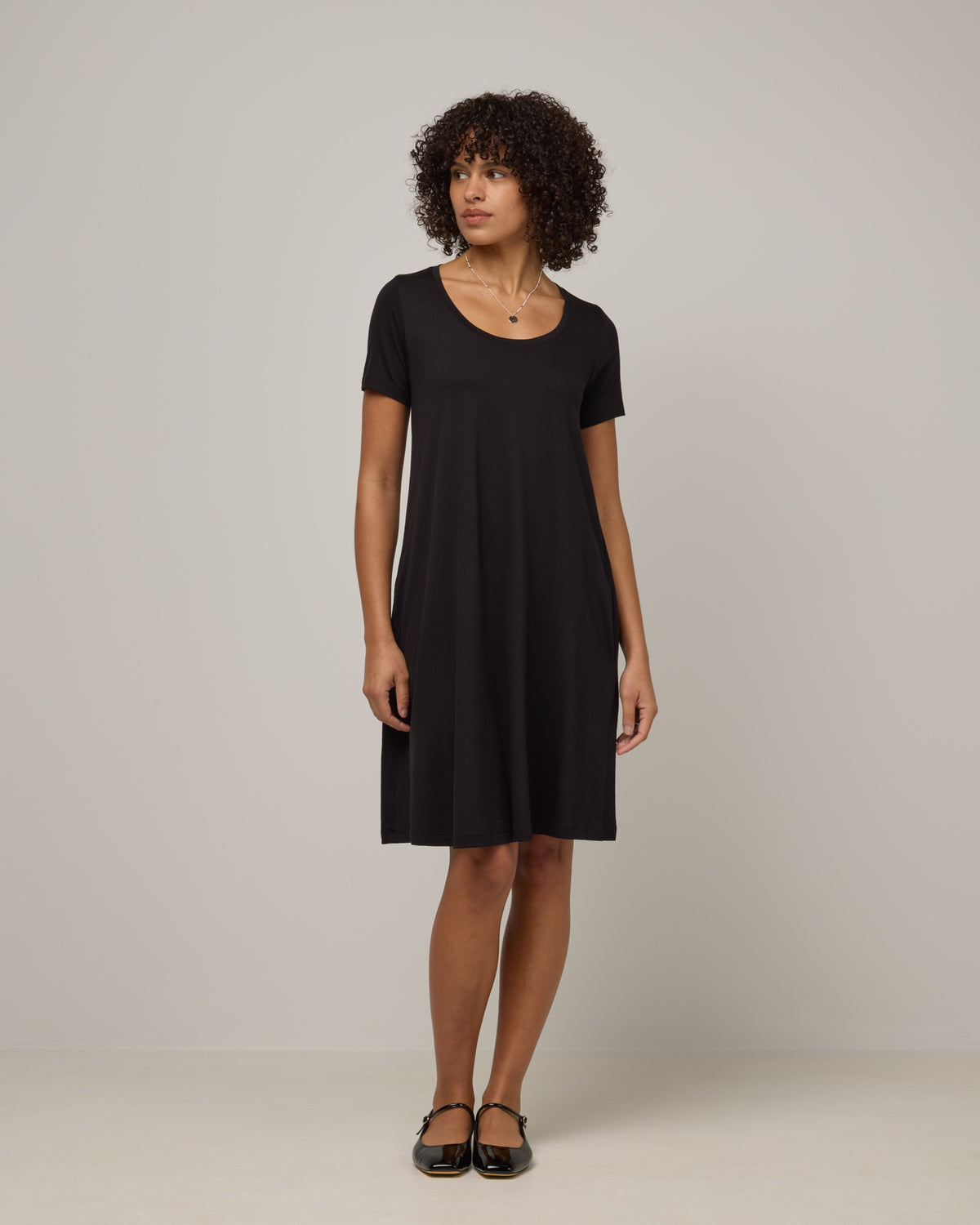 Model wearing Maggie Swing Dress in Black. Maggie Swing Dress is a merino wool short sleeve, scoop neck, knee length swing dress with pockets available in sizes XS-3X Regular, XS-3X Long.