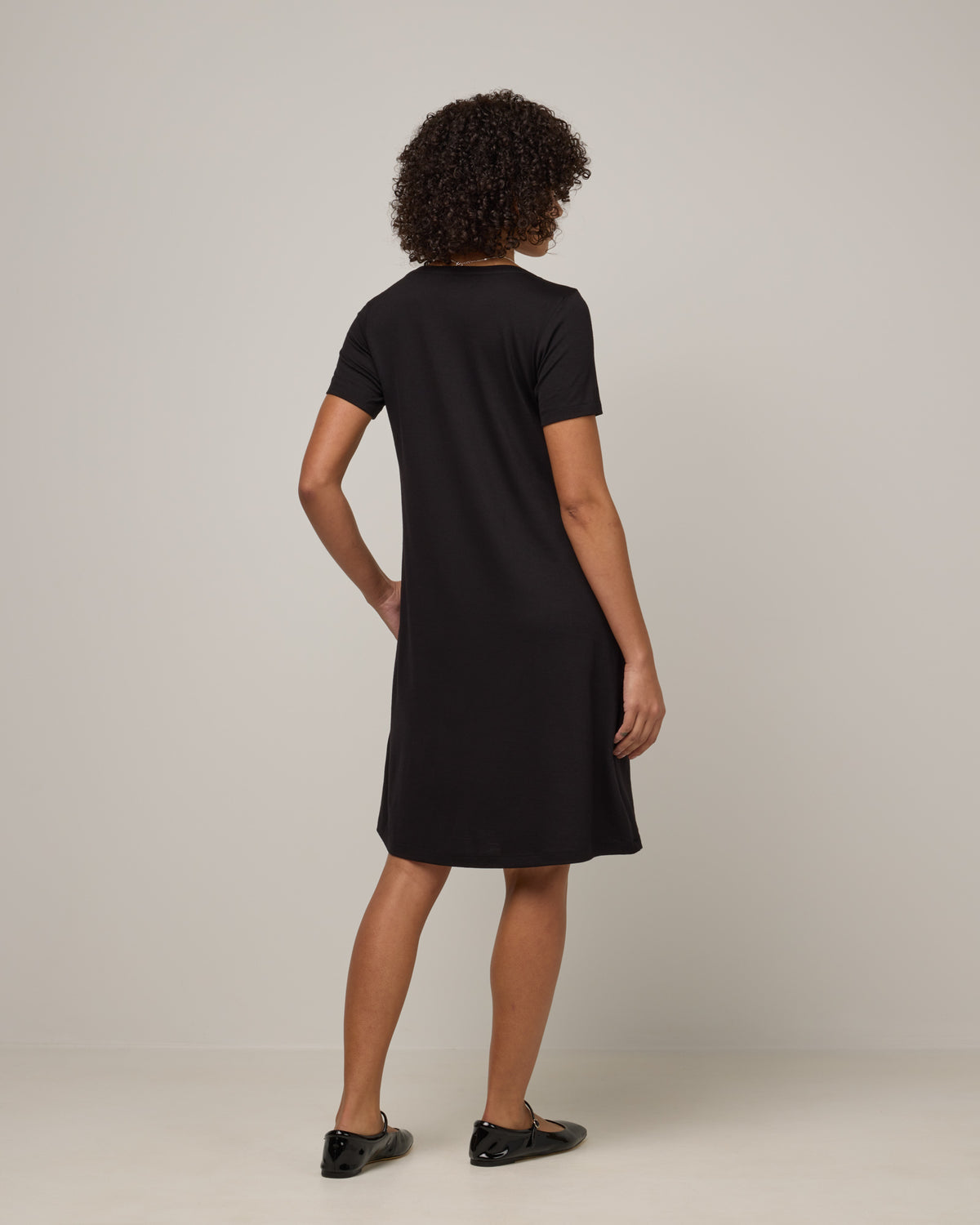 Model wearing Maggie Swing Dress in Black. Maggie Swing Dress is a merino wool short sleeve, scoop neck, knee length swing dress with pockets available in sizes XS-3X Regular, XS-3X Long.