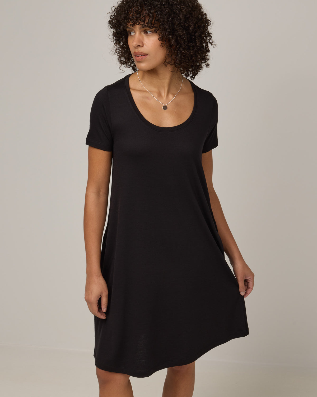 Model wearing Maggie Swing Dress in Black. Maggie Swing Dress is a merino wool short sleeve, scoop neck, knee length swing dress with pockets available in sizes XS-3X Regular, XS-3X Long.