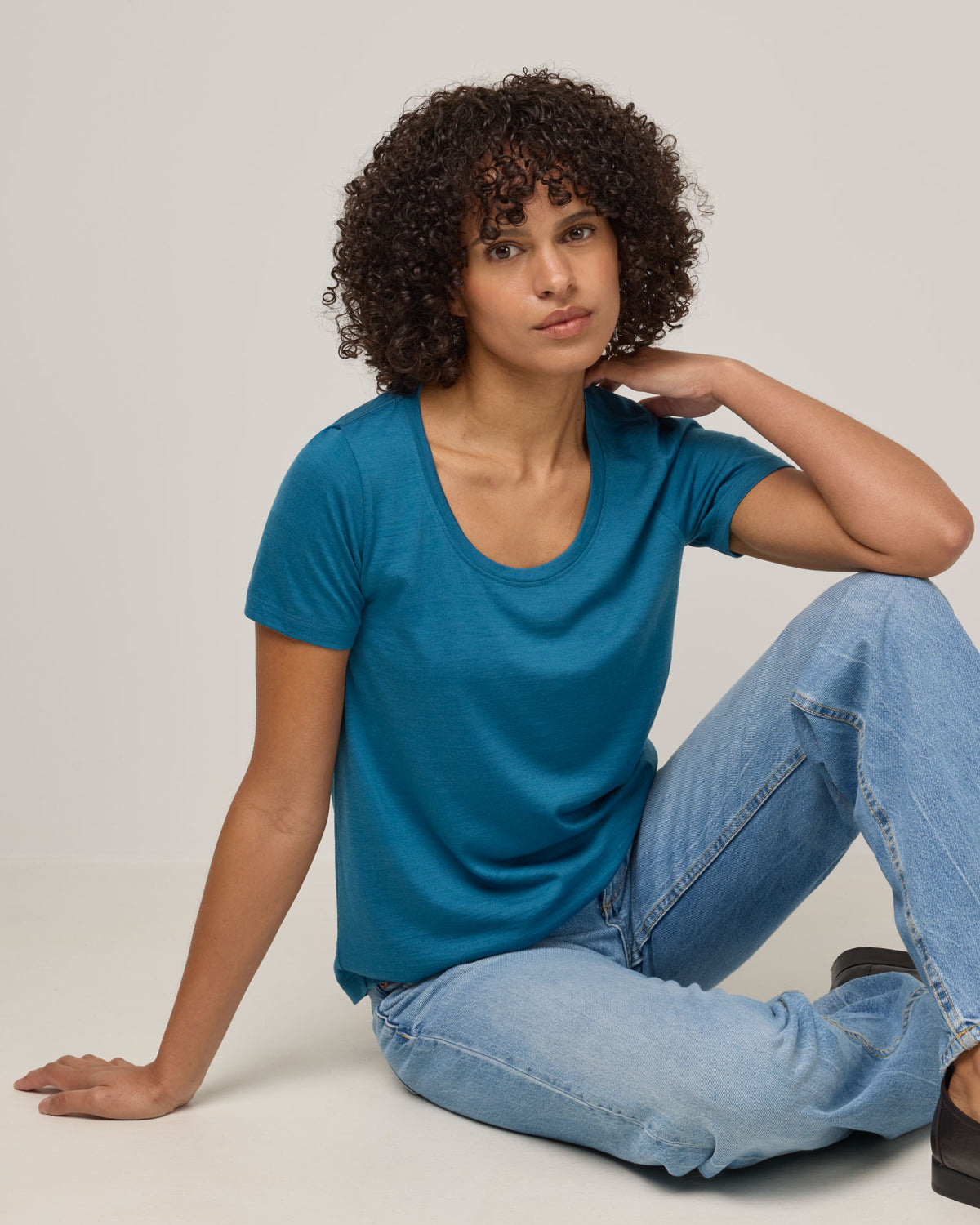 Model wearing Stella Signature Scoop Neck Tee in Ocean Teal, a medium blue-green color. Stella Signature Scoop Neck Tee is a merino wool short sleeve, scoop neck, relaxed fit tee available in sizes XS-3X.