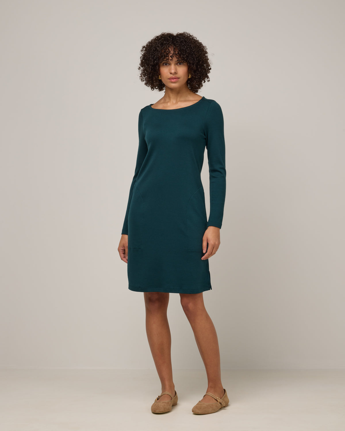 Model wearing Margo Shift Dress in Pine, a saturated forest green color. Margo Shift Dress is a merino wool long sleeve, boatneck, knee length shift dress with pockets available in sizes XS-3X Regular, S-3X Long.