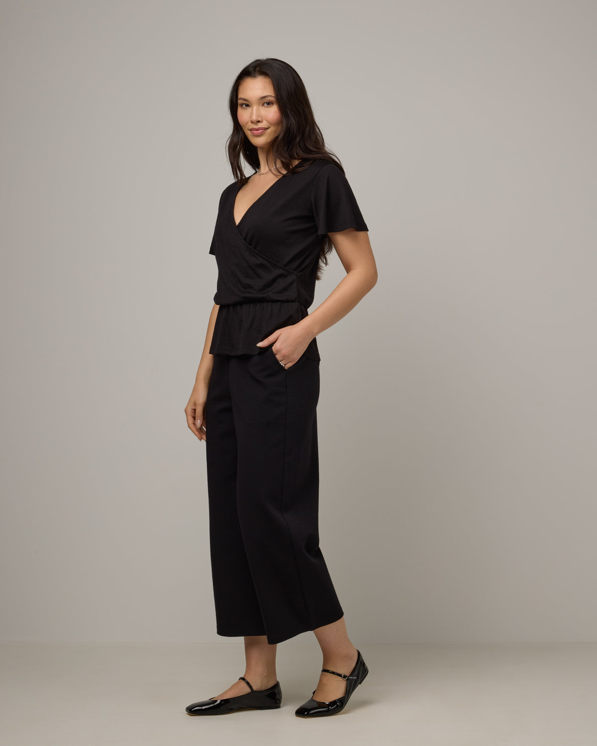 Model wearing Jeanne Flutter Sleeve Top in Black. Jeanne Flutter Sleeve Top is a merino wool short sleeve, reversible, regular fit top available in sizes XS-XXL.