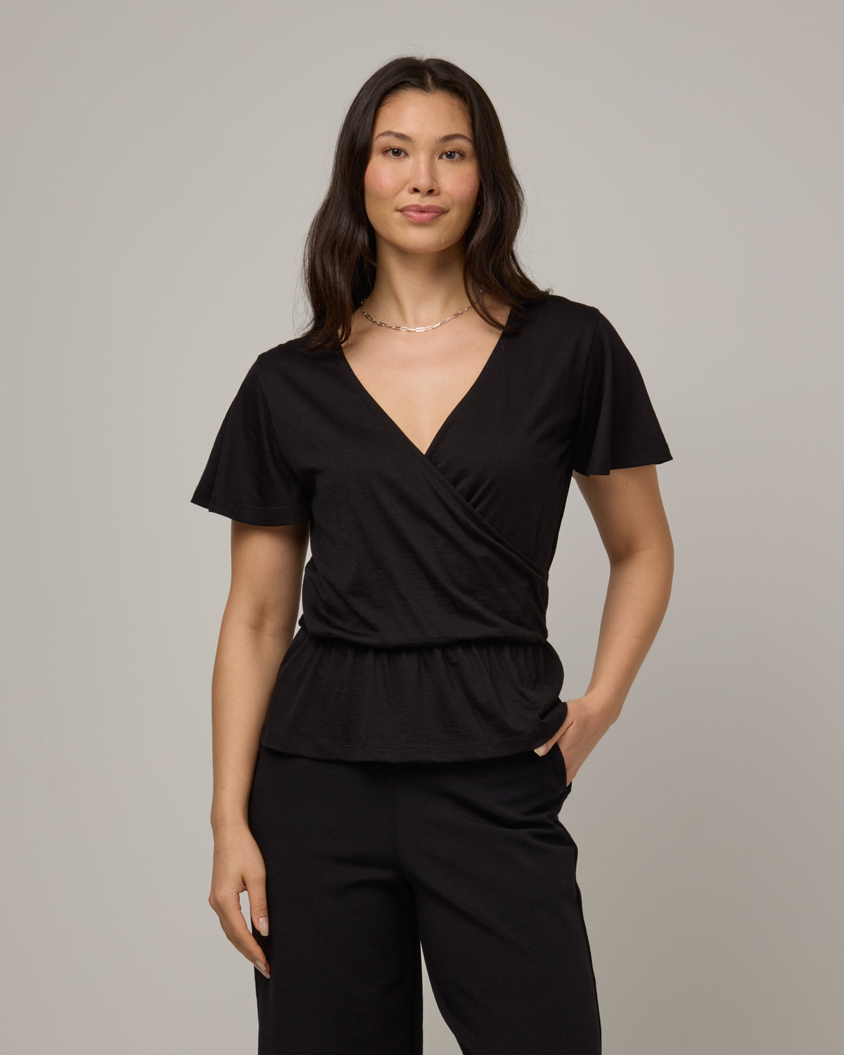 Model wearing Jeanne Flutter Sleeve Top in Black. Jeanne Flutter Sleeve Top is a merino wool short sleeve, reversible, regular fit top available in sizes XS-XXL.