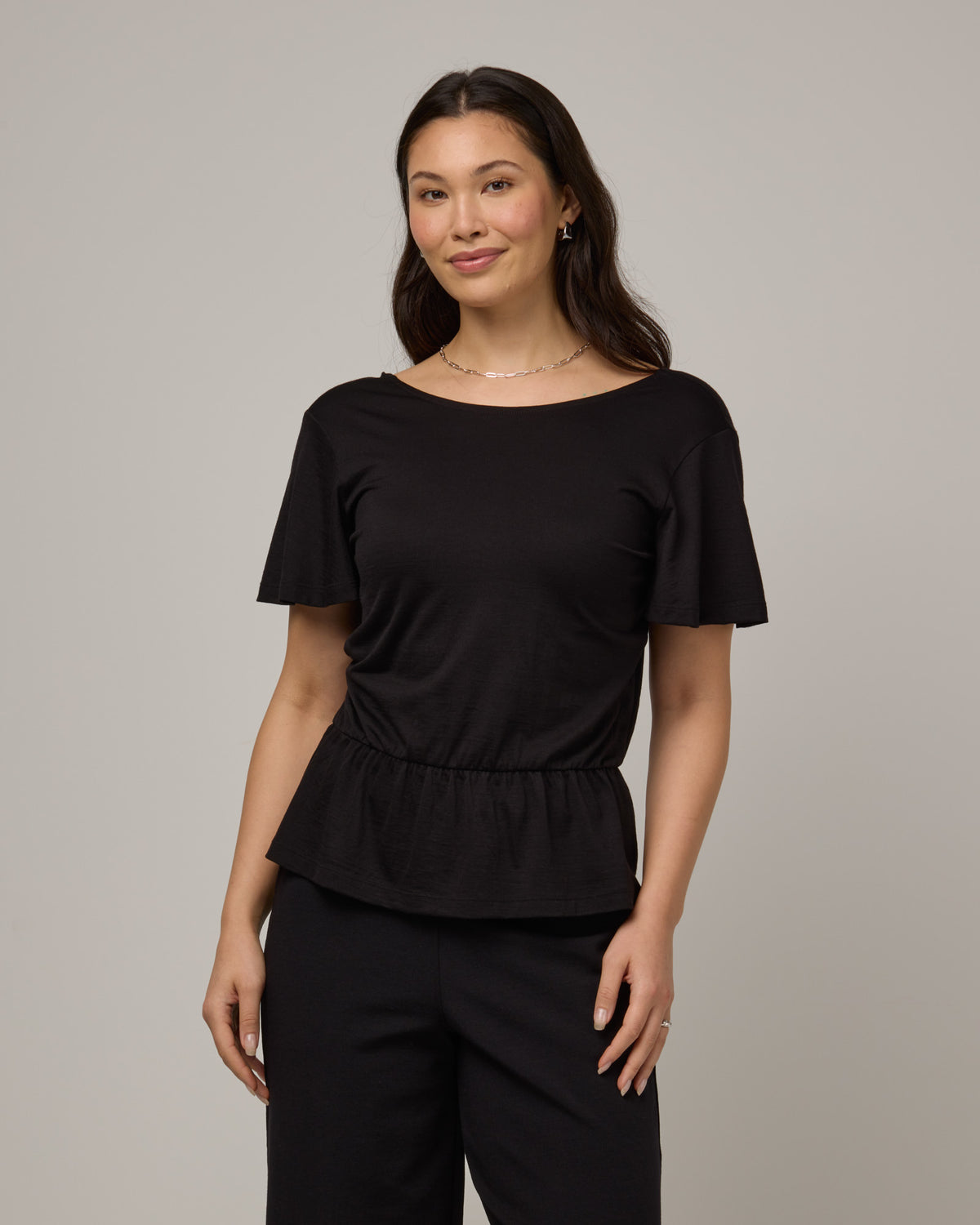 Model wearing Jeanne Flutter Sleeve Top in Black. Jeanne Flutter Sleeve Top is a merino wool short sleeve, reversible, regular fit top available in sizes XS-XXL.