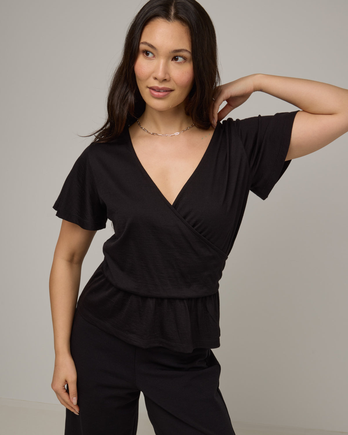 Model wearing Jeanne Flutter Sleeve Top in Black. Jeanne Flutter Sleeve Top is a merino wool short sleeve, reversible, regular fit top available in sizes XS-XXL.