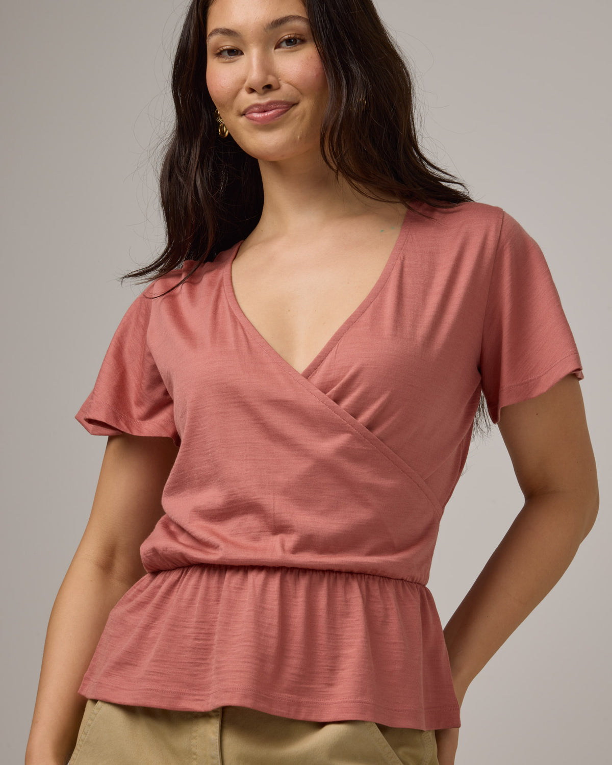 Model wearing Jeanne Flutter Sleeve Top in Vintage Rose, a soft muted pink color. Jeanne Flutter Sleeve Top is a merino wool short sleeve, reversible, regular fit top available in sizes XS-XXL.