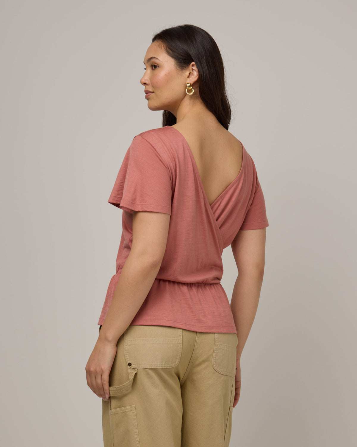 Model wearing Jeanne Flutter Sleeve Top in Vintage Rose, a soft muted pink color. Jeanne Flutter Sleeve Top is a merino wool short sleeve, reversible, regular fit top available in sizes XS-XXL.