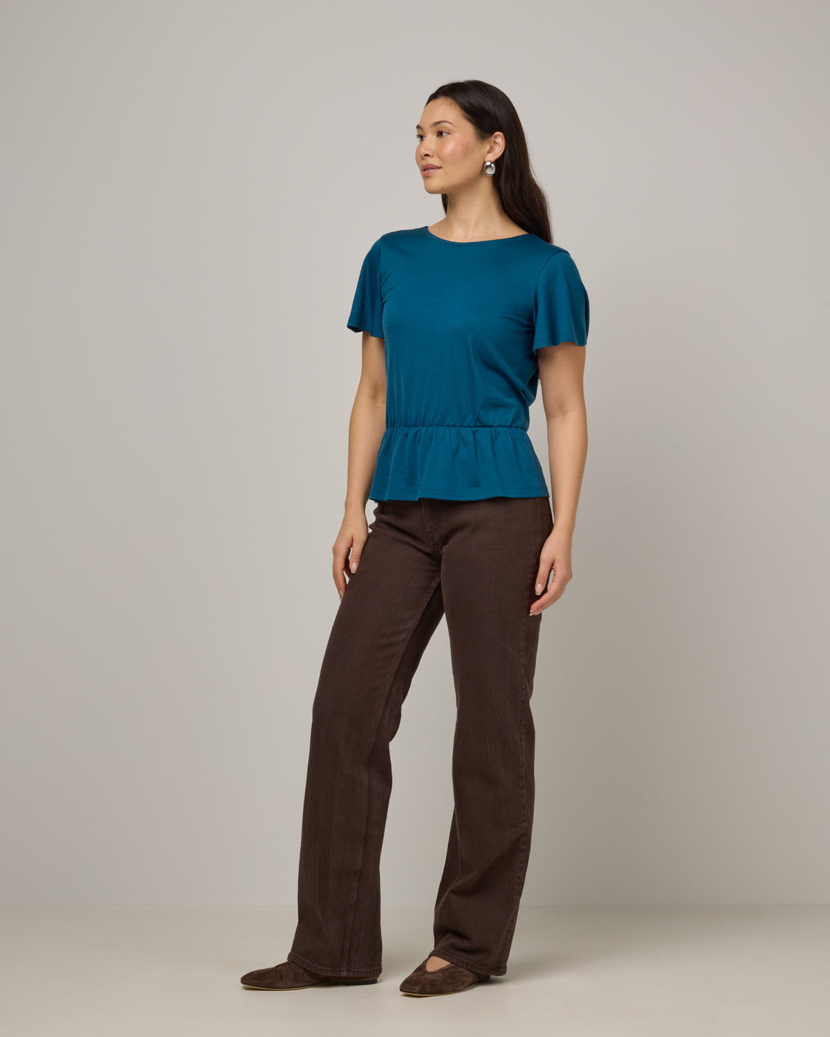 Model wearing Jeanne Flutter Sleeve Top in Ocean Teal, a medium blue-green color. Jeanne Flutter Sleeve Top is a merino wool short sleeve, reversible, regular fit top available in sizes XS-XXL.