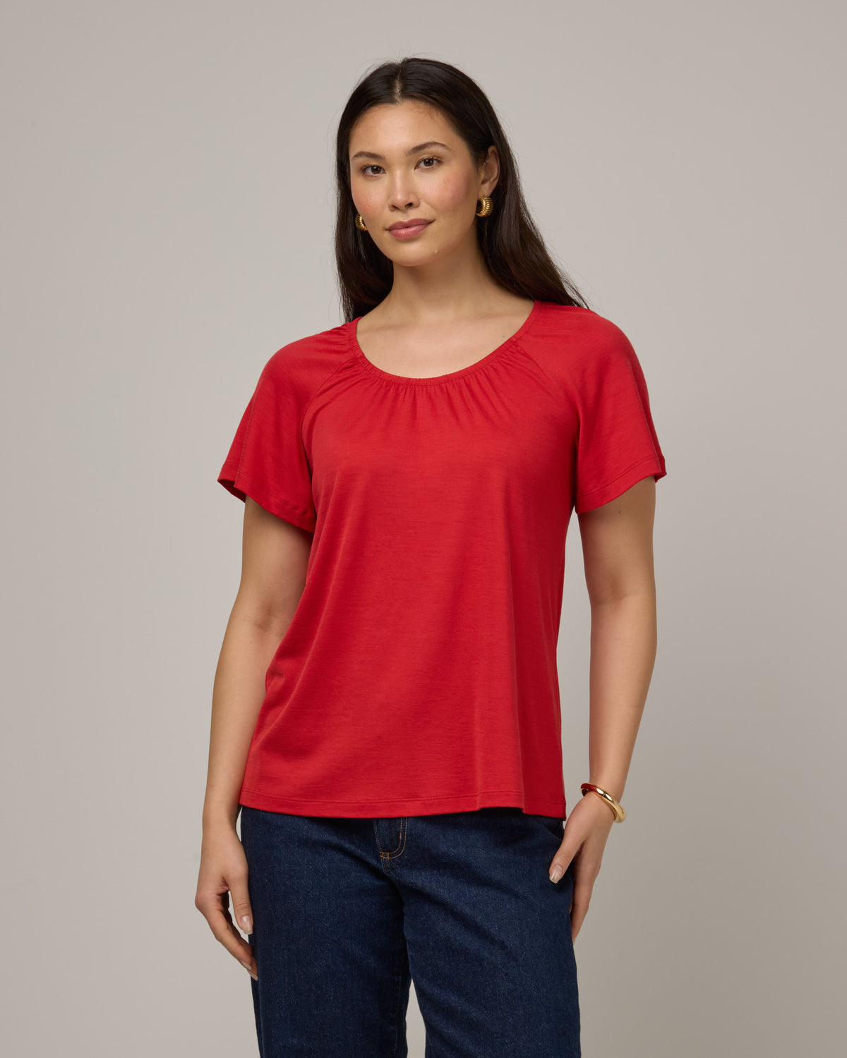 Model wearing Lilah Signature Gathered Neck Tee in Fruit Punch, a vivid red-orange color. Lilah Signature Gathered Neck Tee is a merino wool short sleeve, scoop neck, relaxed fit tee available in sizes XS-3X.