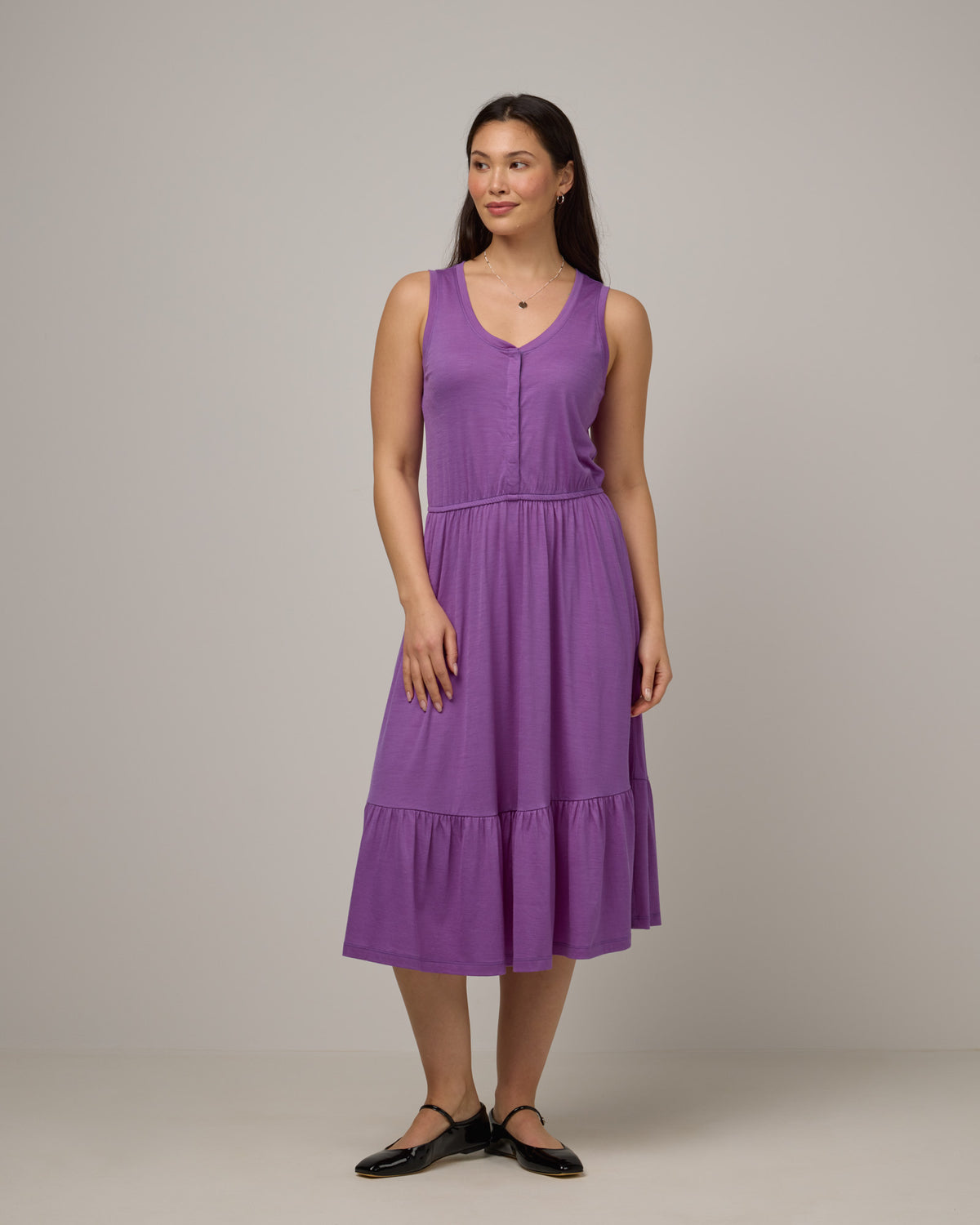 Model wearing Grace Tiered Dress in Purple Pansy, a bright, saturated purple color. Grace Tiered Dress is a merino wool sleeveless, scoop neck, midi fit & flare dress with pockets available in sizes XS-3X.