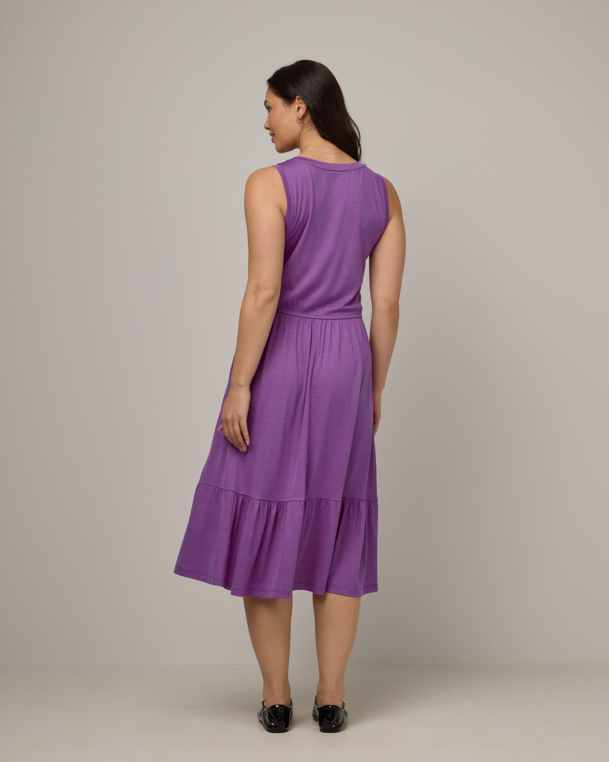Model wearing Grace Tiered Dress in Purple Pansy, a bright, saturated purple color. Grace Tiered Dress is a merino wool sleeveless, scoop neck, midi fit & flare dress with pockets available in sizes XS-3X.