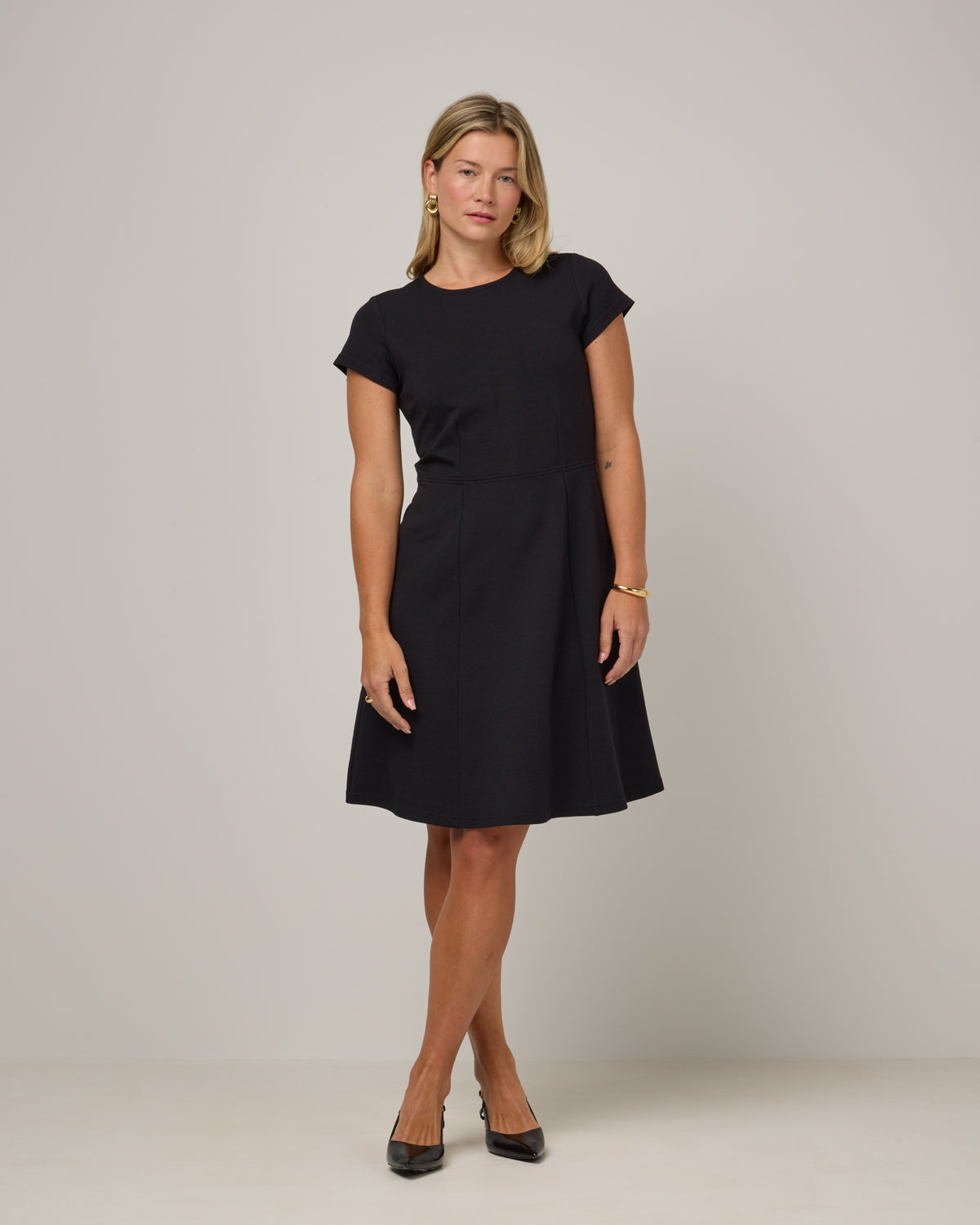 Model wearing Anais Fit & Flare Dress in Black. Anais Fit & Flare Dress is a merino wool short sleeve, square neck, knee length fit & flare dress with pockets available in sizes XS-XXL.