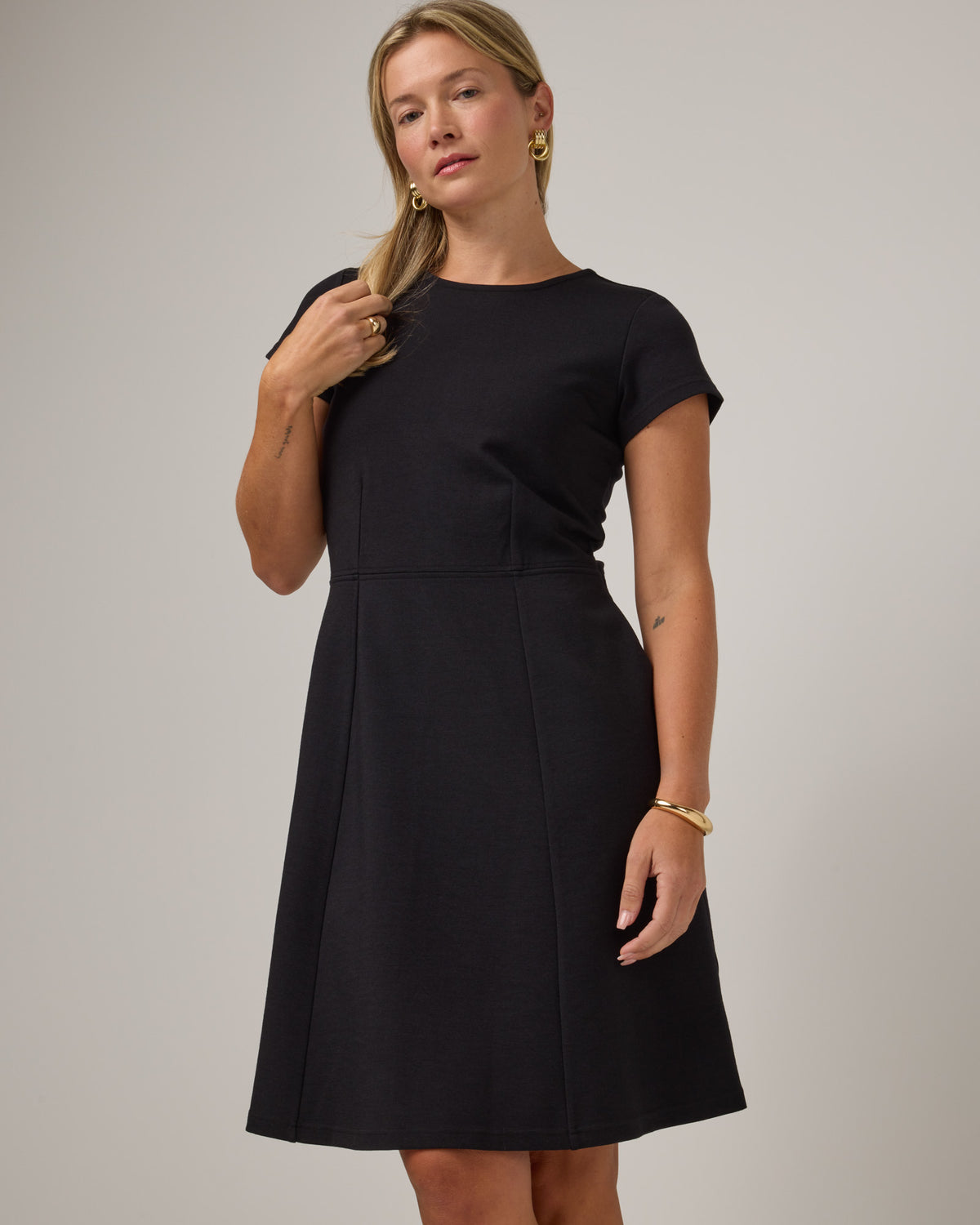 Model wearing Anais Fit & Flare Dress in Black. Anais Fit & Flare Dress is a merino wool short sleeve, square neck, knee length fit & flare dress with pockets available in sizes XS-XXL.