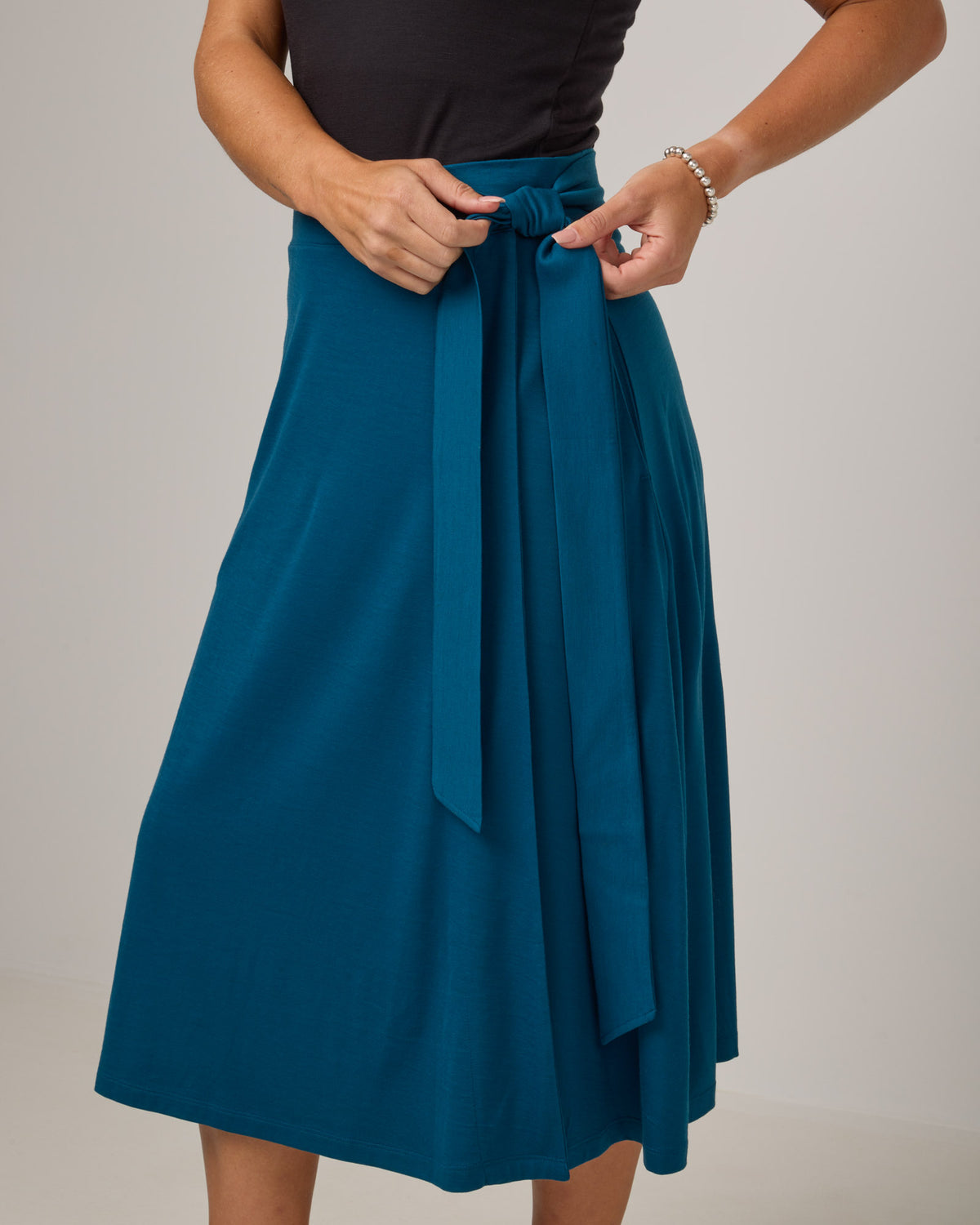 Model wearing Skye Wrap Skirt in Ocean Teal, a medium blue-green color. Skye Wrap Skirt is a merino wool midi length skirt with pockets available in sizes XS-3X.