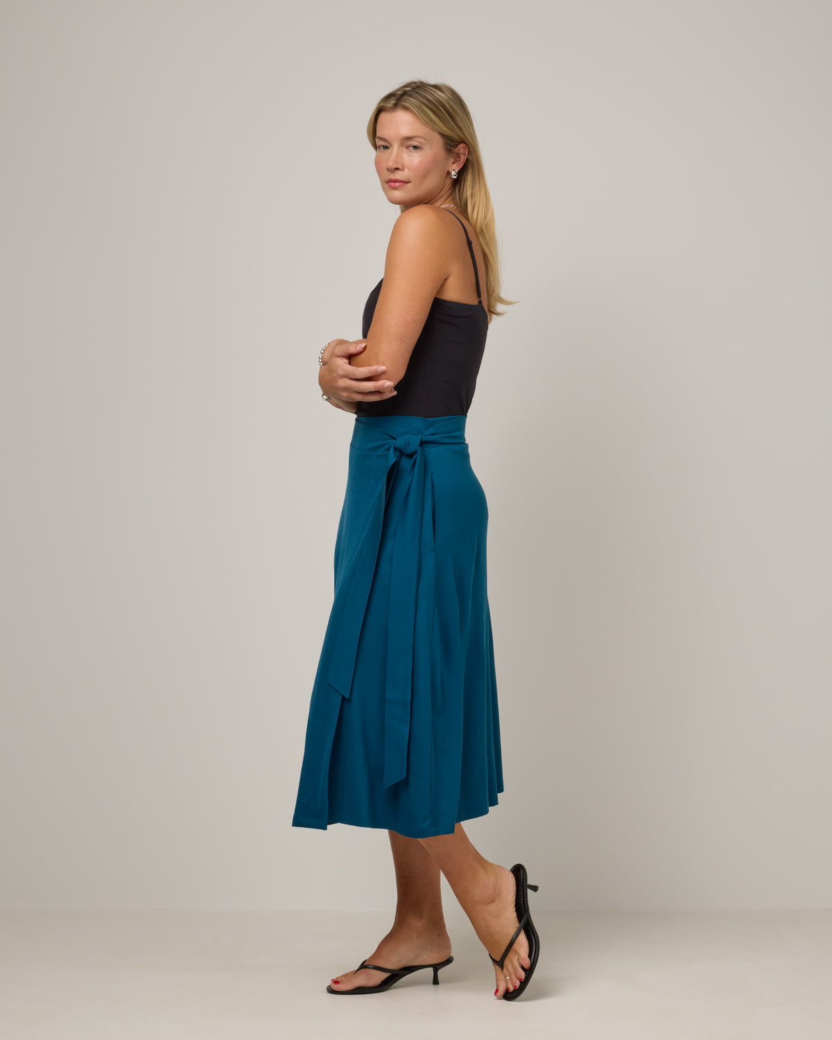 Model wearing Skye Wrap Skirt in Ocean Teal, a medium blue-green color. Skye Wrap Skirt is a merino wool midi length skirt with pockets available in sizes XS-3X.