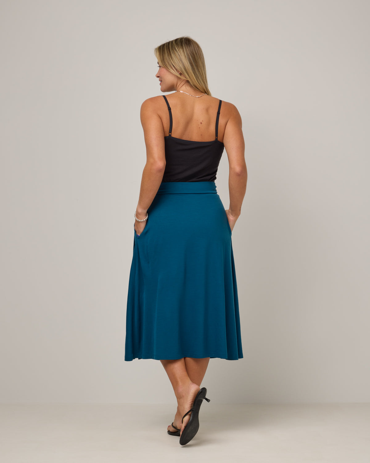 Model wearing Skye Wrap Skirt in Ocean Teal, a medium blue-green color. Skye Wrap Skirt is a merino wool midi length skirt with pockets available in sizes XS-3X.