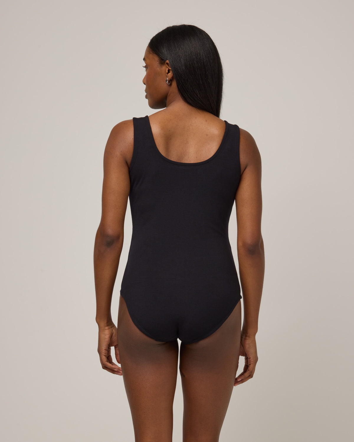 Model wearing Britt Bodysuit in Black. Britt Bodysuit is a merino wool slim fit, sleeveless, scoop neck bodysuit available in sizes XS-XXL.