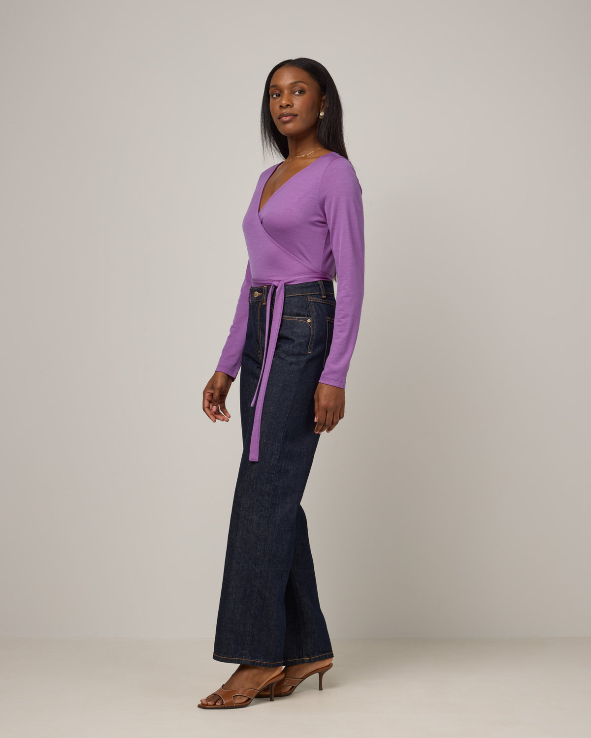 Model wearing Natalia Wrap Top in Purple Pansy, a bright, saturated purple color. Natalia Wrap Top is a merino wool long sleeve, v-neck, slim fit top available in sizes XS-3X.