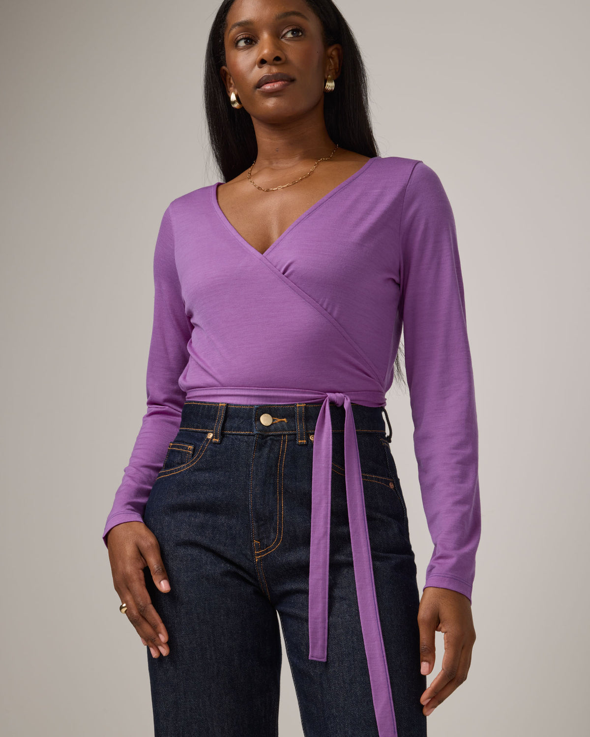 Model wearing Natalia Wrap Top in Purple Pansy, a bright, saturated purple color. Natalia Wrap Top is a merino wool long sleeve, v-neck, slim fit top available in sizes XS-3X.