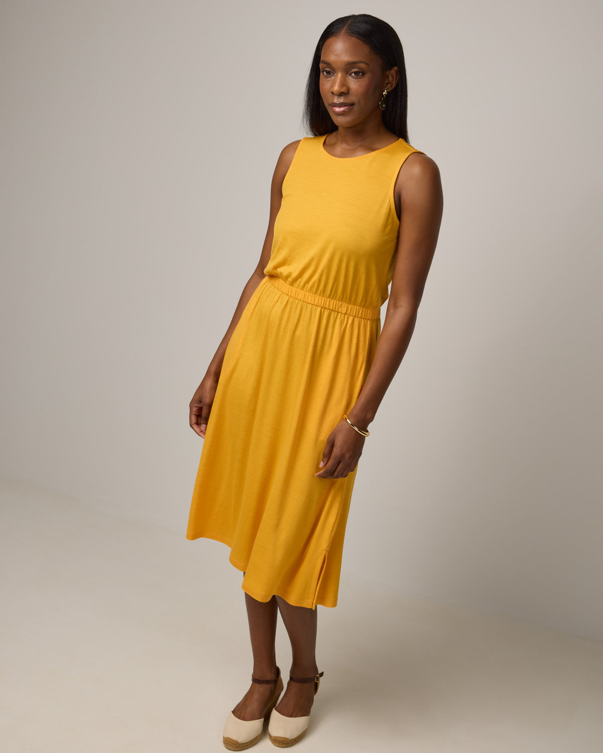 Model wearing Sofia Fit & Flare Dress in Mango, a sunshine yellow-orange color. Sofia Fit & Flare Dress is a merino wool sleeveless, crew neck, midi fit & flare dress with pockets available in sizes XS-XXL.