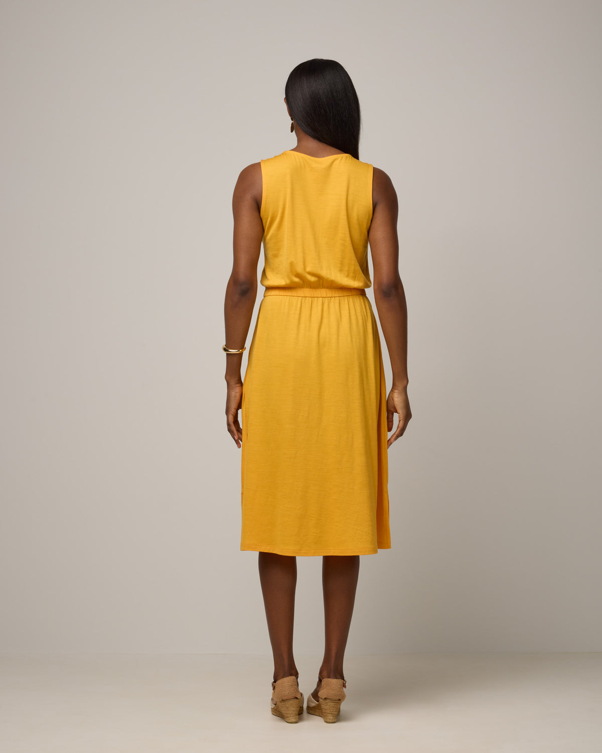 Model wearing Sofia Fit & Flare Dress in Mango, a sunshine yellow-orange color. Sofia Fit & Flare Dress is a merino wool sleeveless, crew neck, midi fit & flare dress with pockets available in sizes XS-XXL.