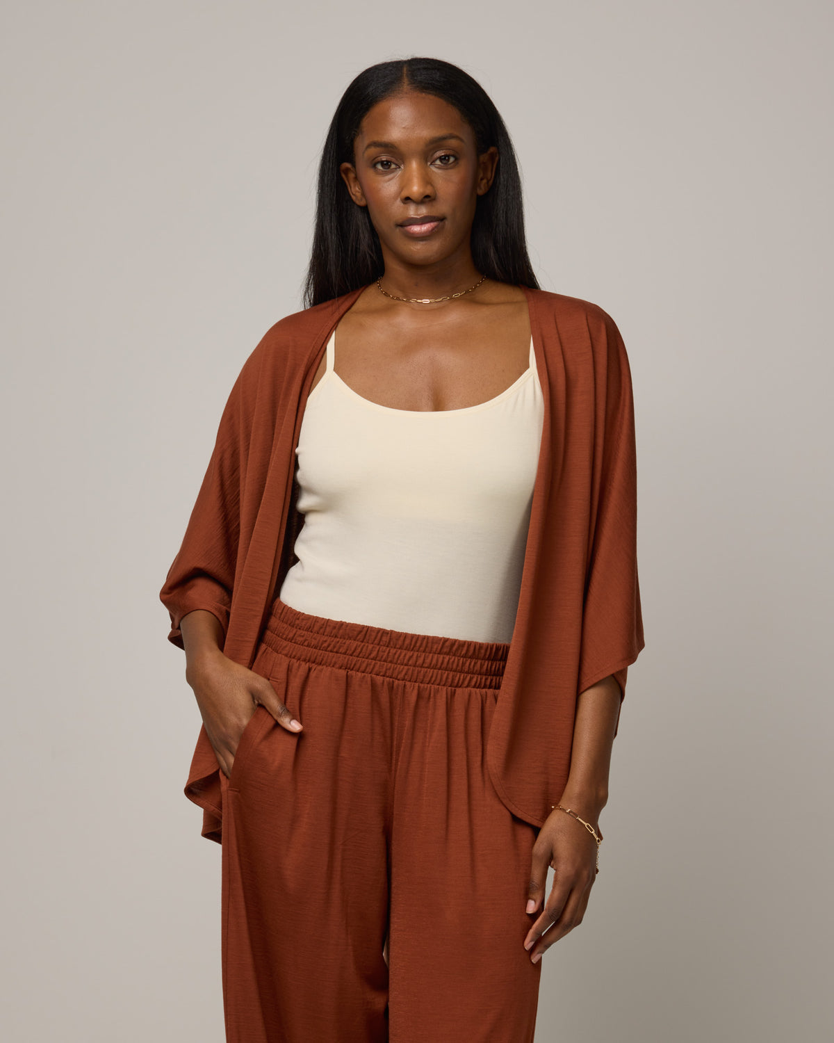 Model wearing Lisbon Shawl Cardigan in Cinnamon, a reddish-brown rust color. Lisbon Shawl Cardigan is a merino wool short sleeve cardigan available in sizes XS/S-2X/3X.