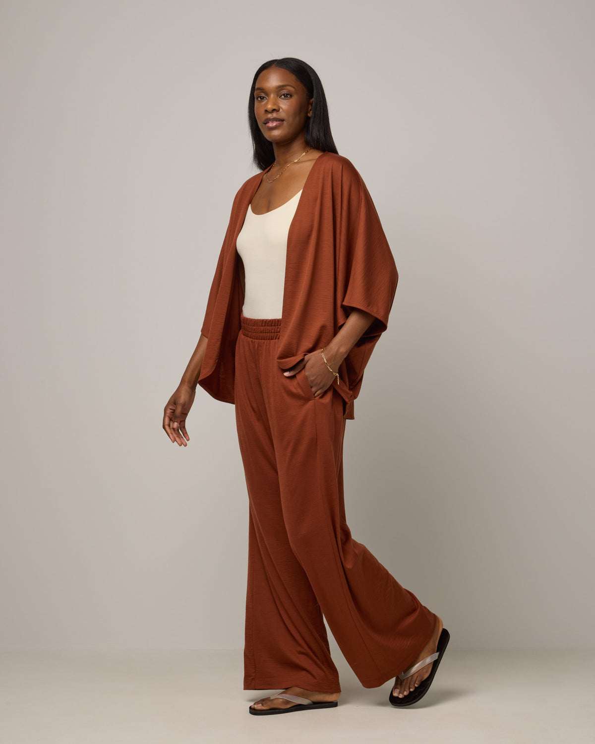 Model wearing Lisbon Shawl Cardigan in Cinnamon, a reddish-brown rust color. Lisbon Shawl Cardigan is a merino wool short sleeve cardigan available in sizes XS/S-2X/3X.