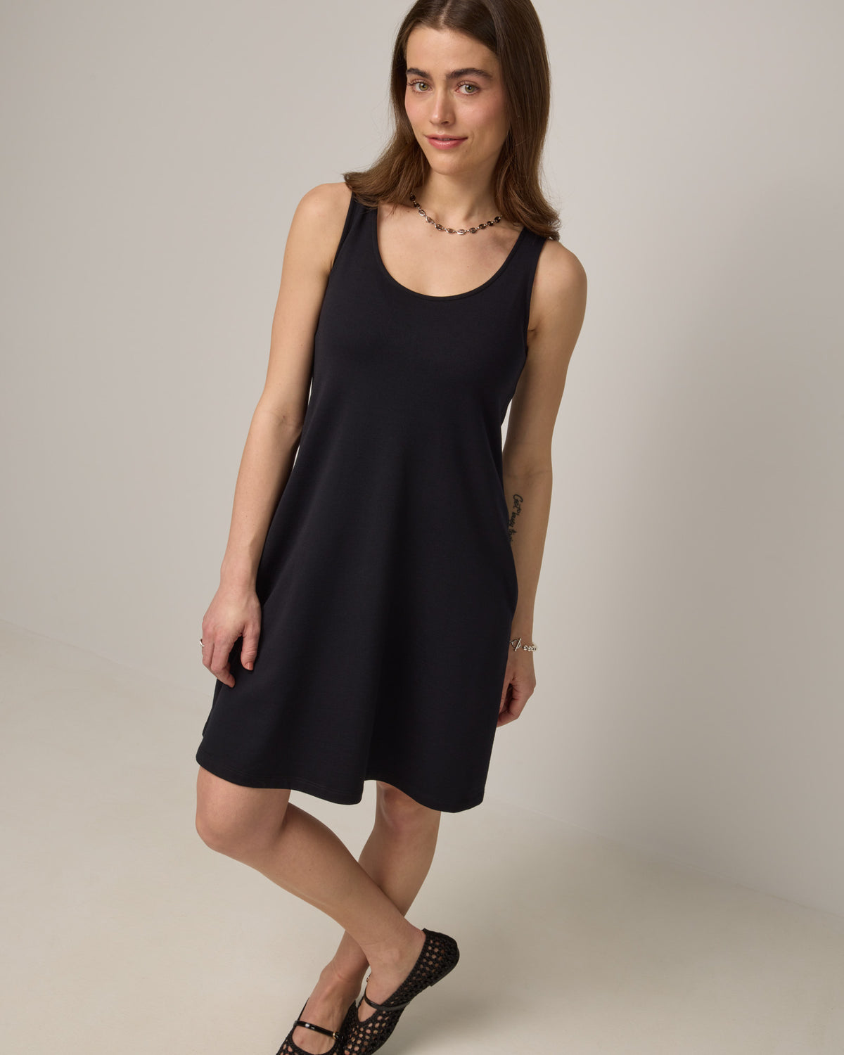 Model wearing Drew Tank Dress in Black. Drew Tank Dress is a merino wool sleeveless, scoop neck, knee length swing dress available in sizes XS-3X. 