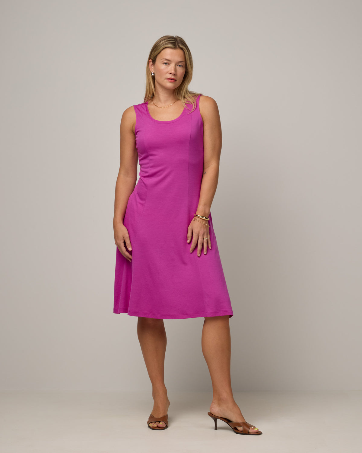 Model wearing Flora Swing Dress in Petunia, a bright fuchsia pink-purple color. Flora Swing Dress is a merino wool sleeveless, scoop neck, knee length swing dress with pockets available in sizes XS-3X.